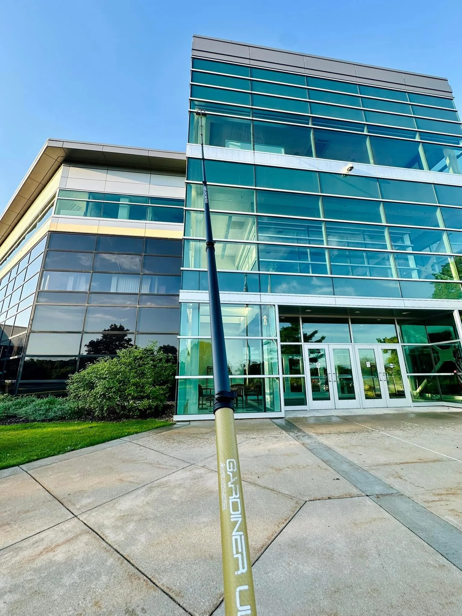 Modern glass building with a sidewalk and a yellow pole in the foreground, clear blue sky.