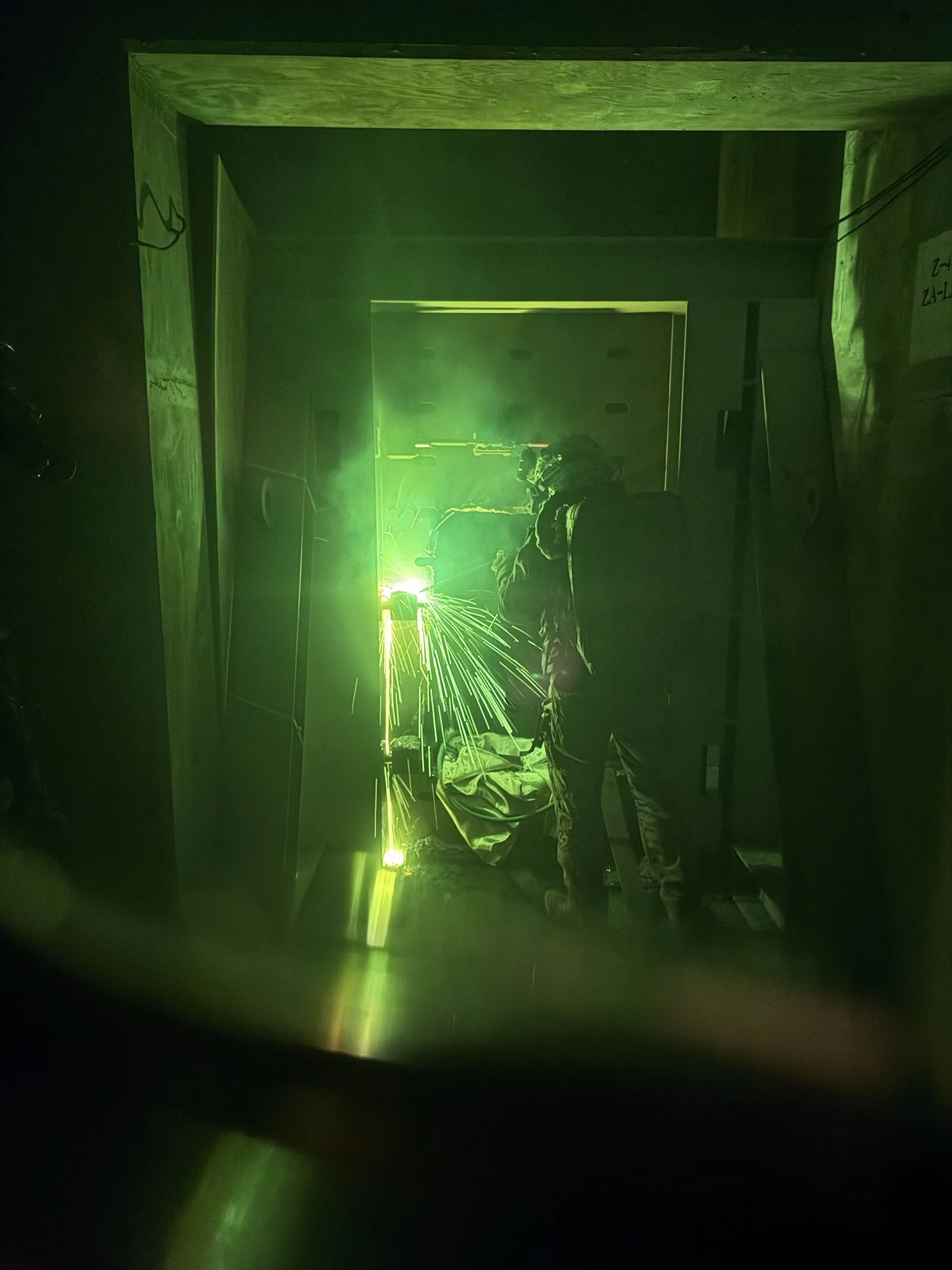 Person welding with a green laser, sparks flying, in an indoor workshop or construction site.