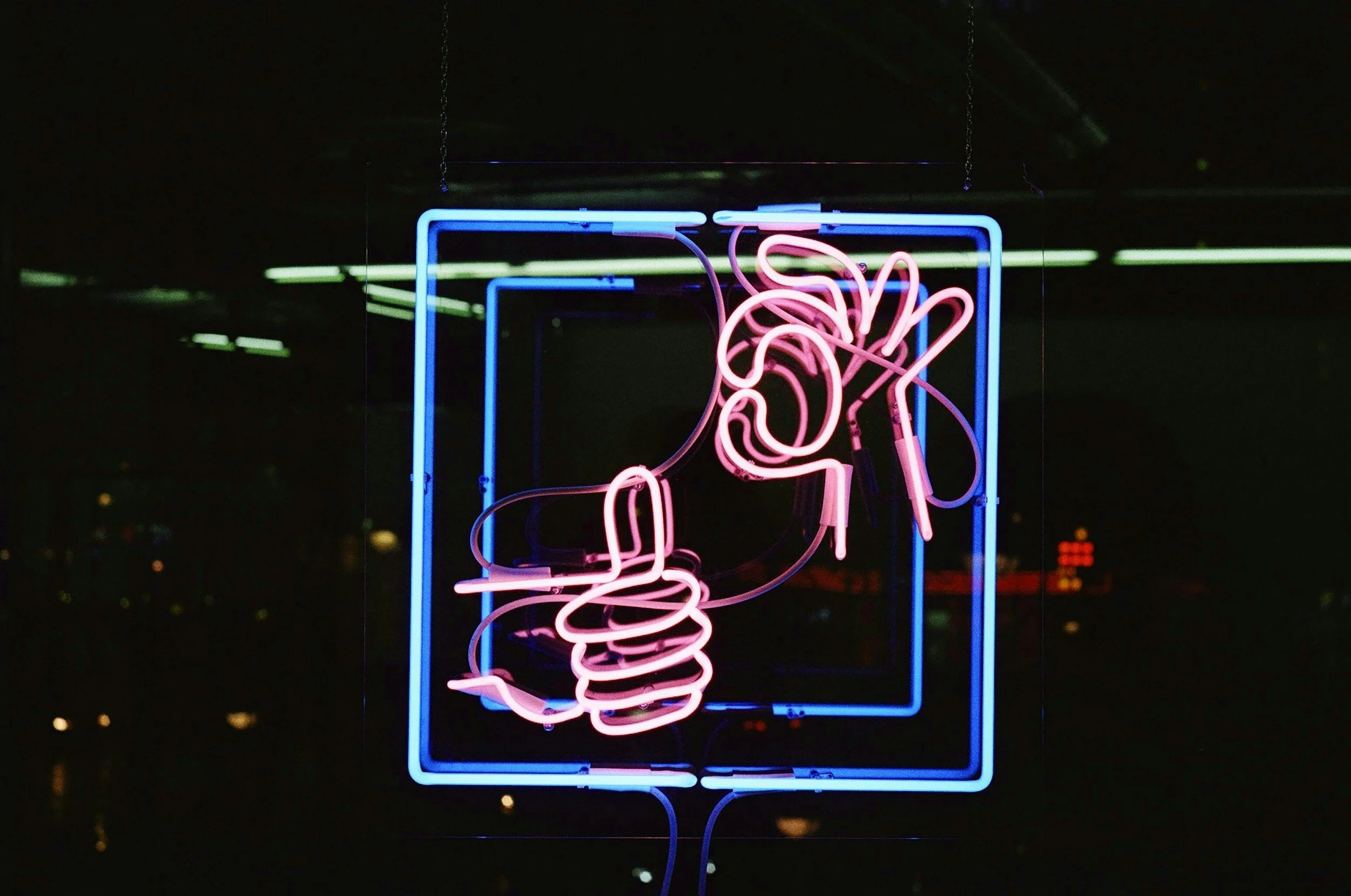 Neon sign depicting a person sitting with their head resting on their hand, in pink and blue neon lights against a dark background.