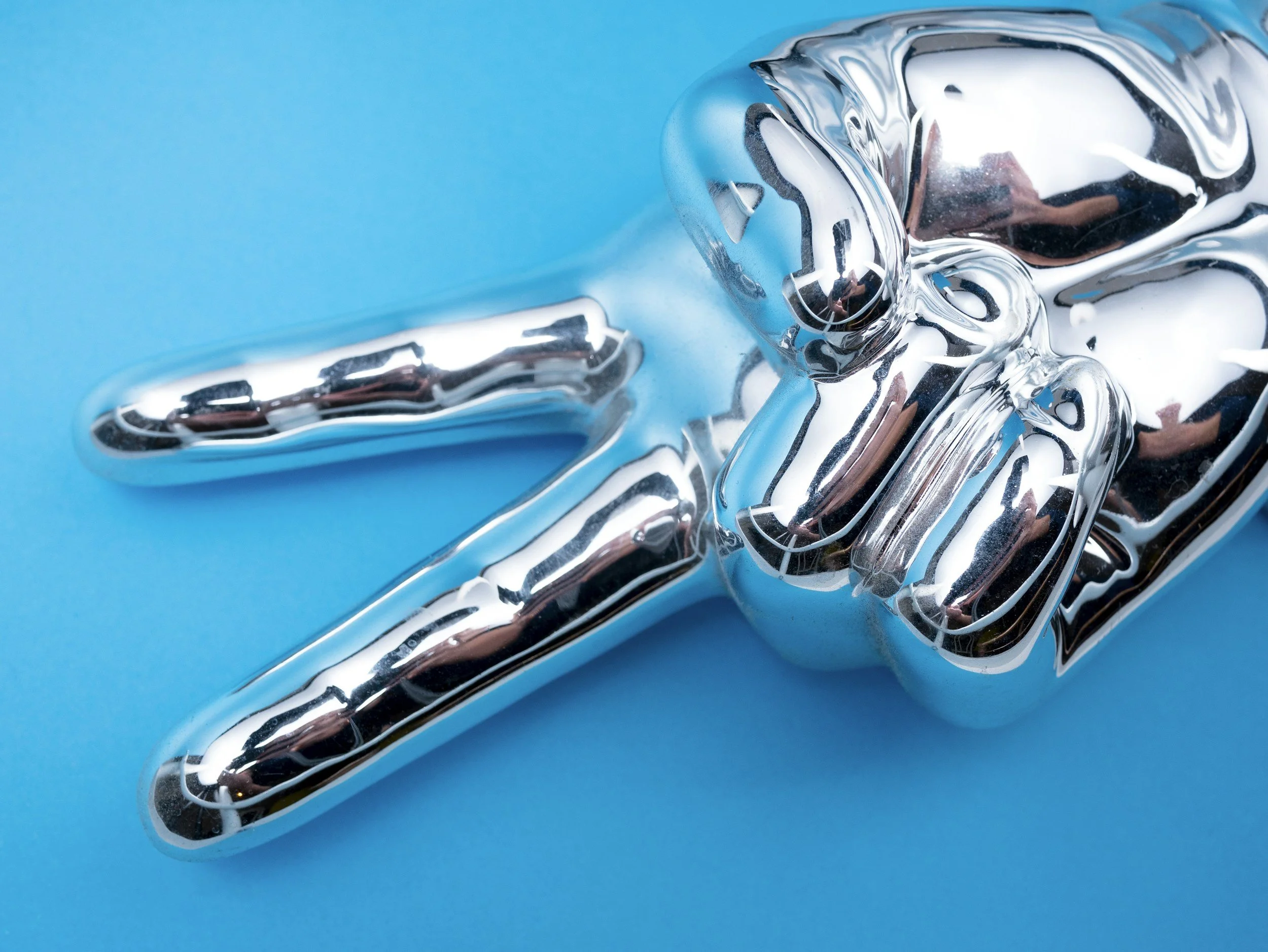 Close-up of a shiny silver balloon shaped like the number four, against a bright blue background.