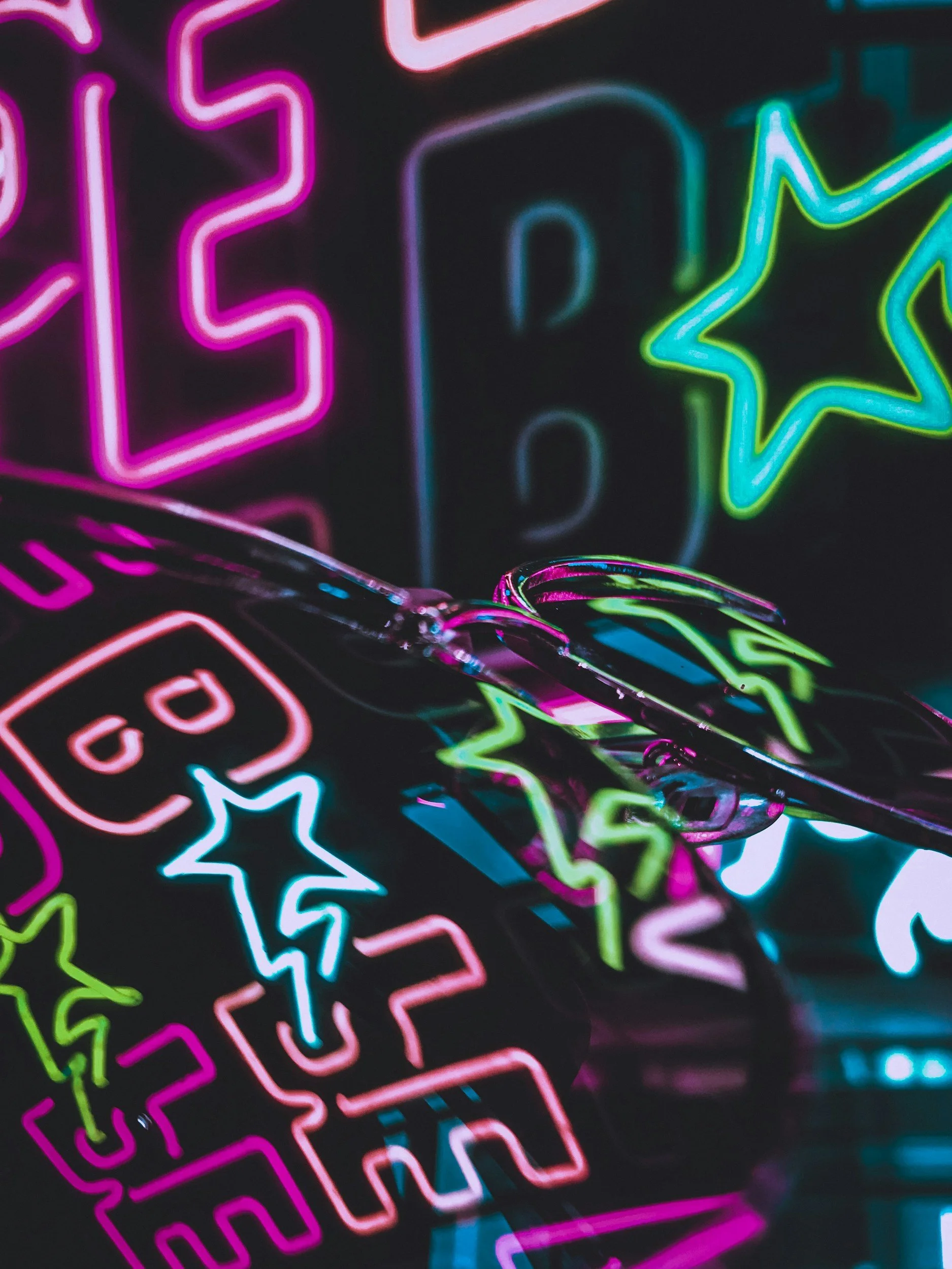 Close-up image of colorful neon signs with the words 'LOVE' and various star and lightning bolt shapes illuminated in green, pink, blue, and purple hues.