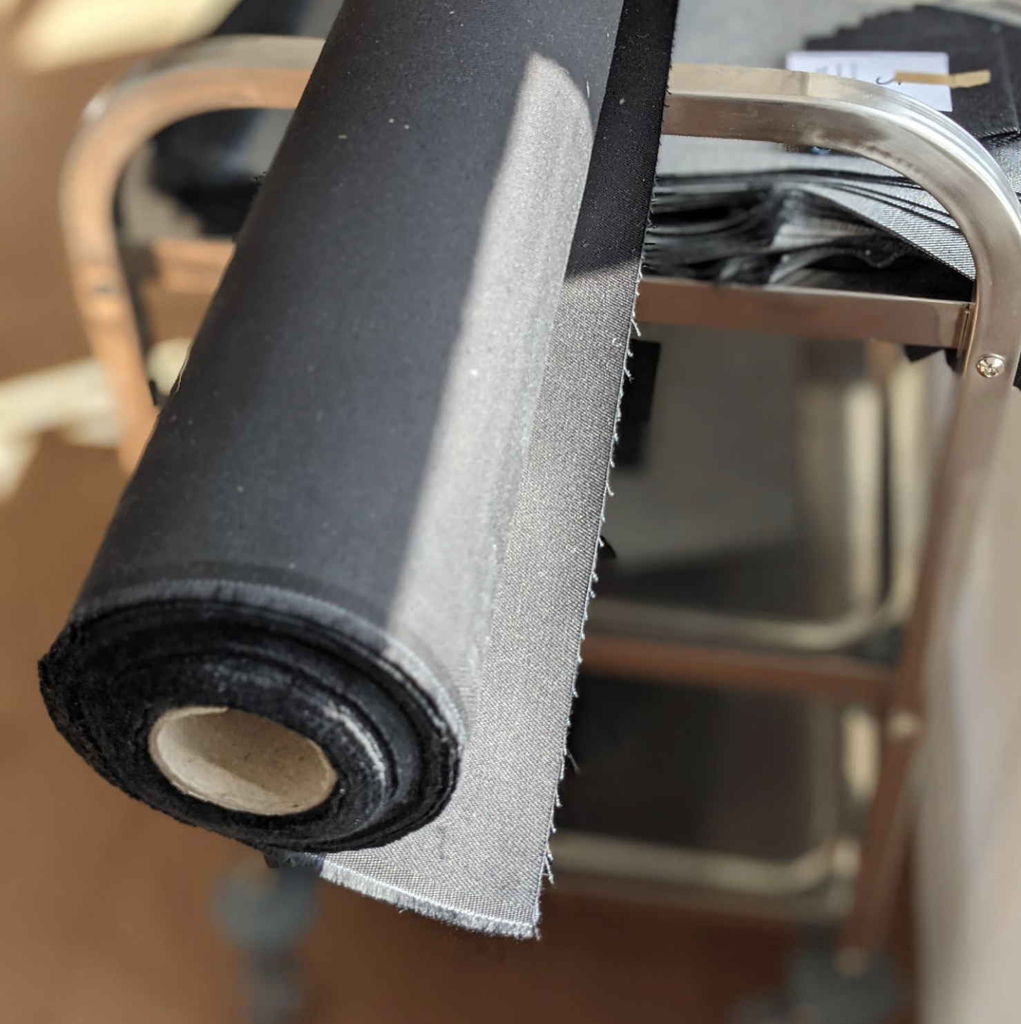 A roll of black fabric or vinyl material on a metal rack, with a partly visible black suitcase in the background.