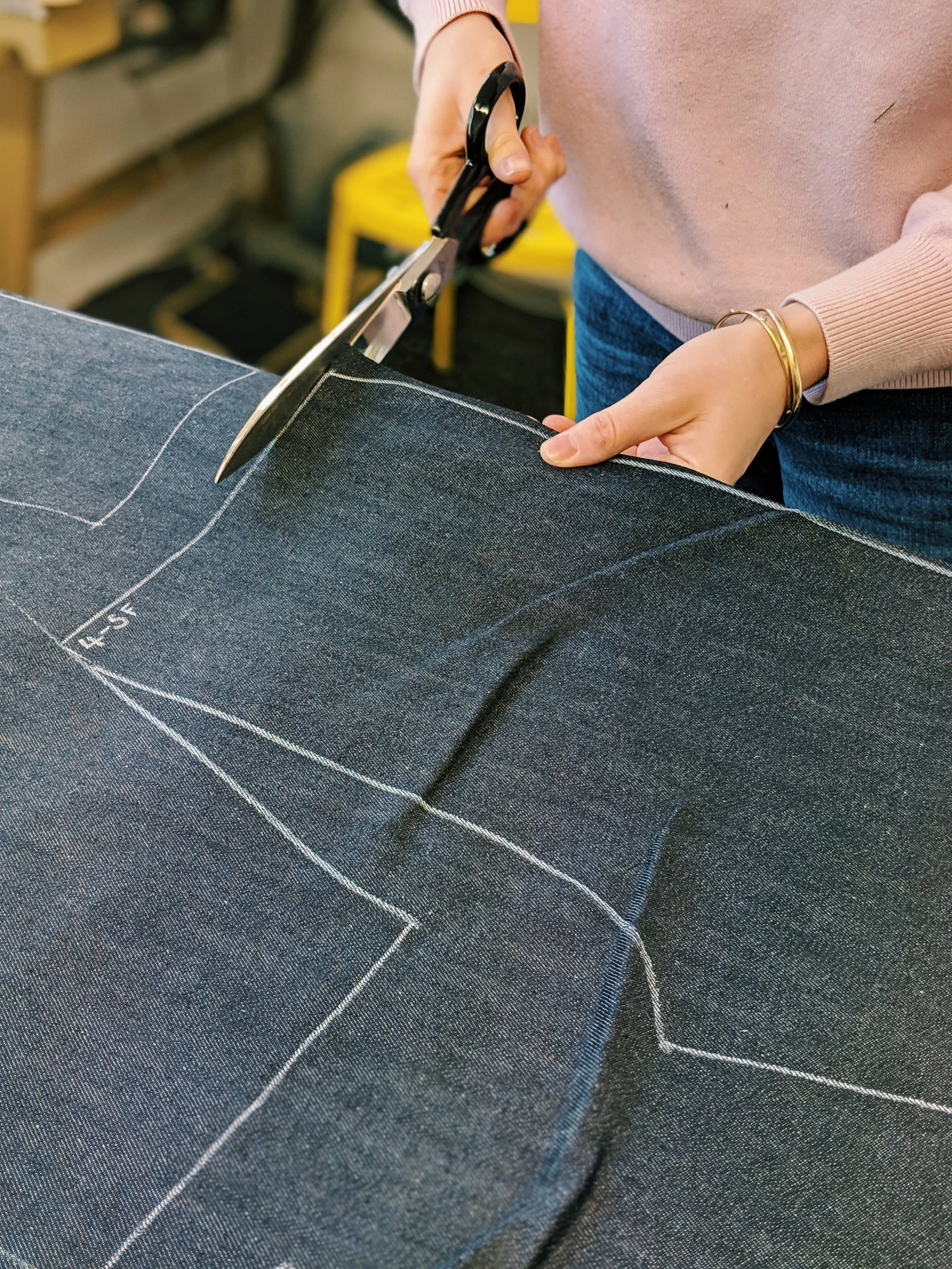 Person cutting dark denim fabric with scissors on a sewing table.