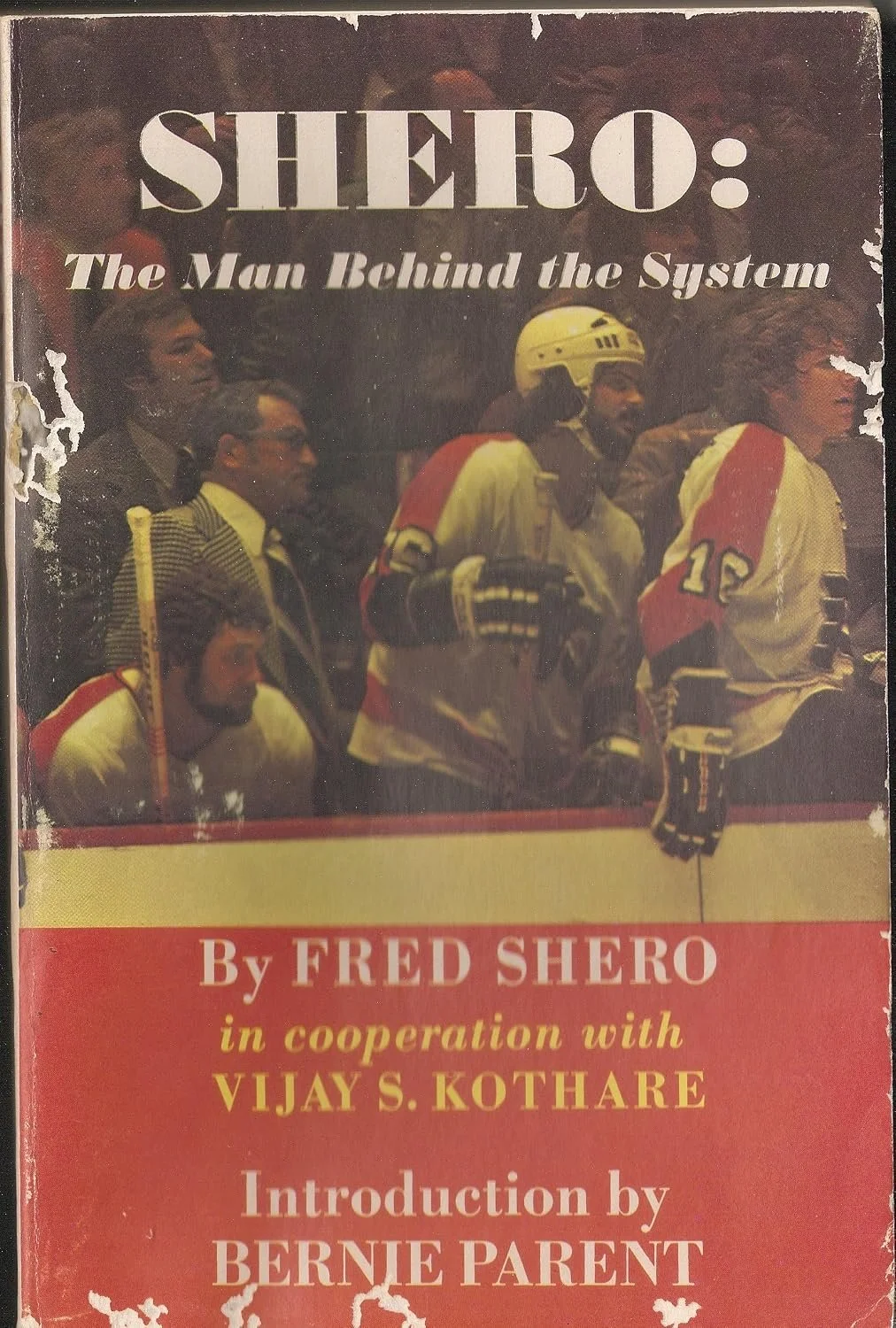 Book cover titled "Shero: The Man Behind the System" by Fred Shero, in cooperation with Vijay S. Kothare, with an introduction by Bernie Parent. The cover features a photo of hockey players and coaches in uniform, some standing and others sitting, with a worn, vintage appearance.