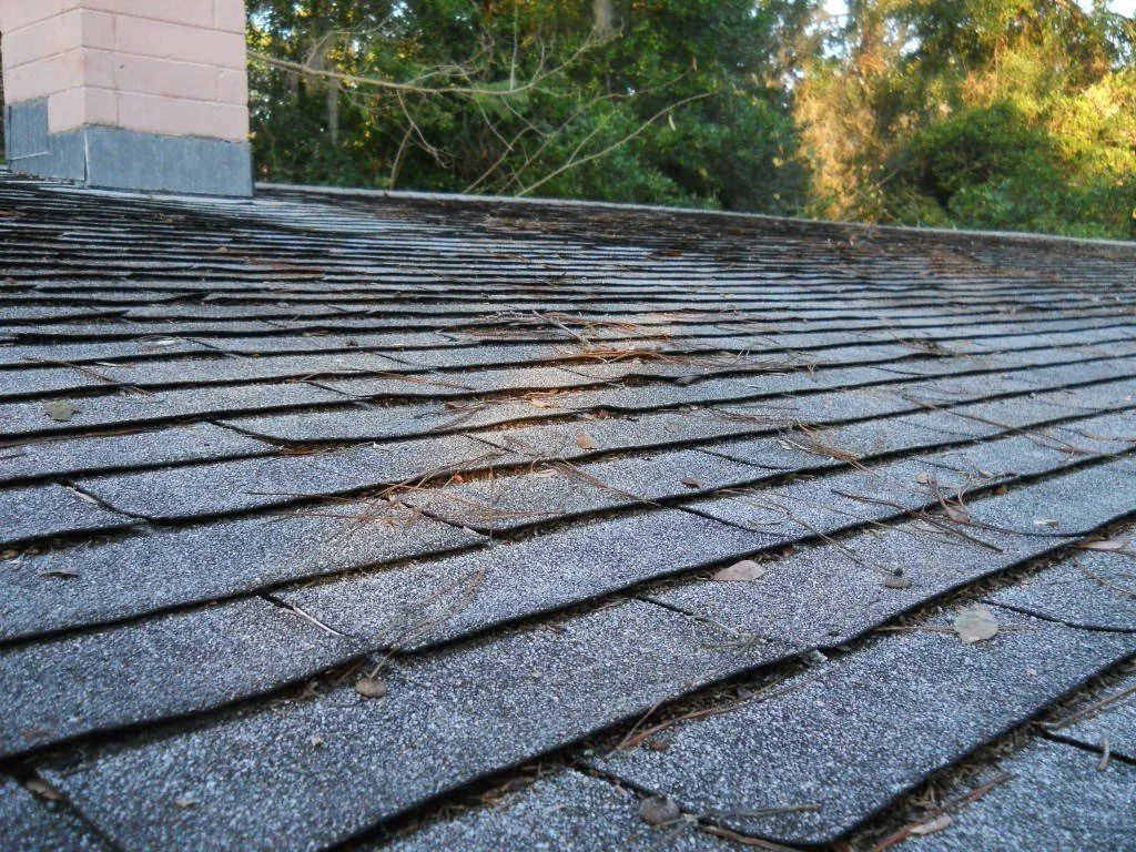 photo shows roof with old and damaged shingles