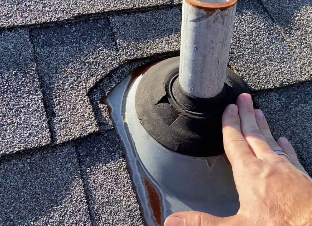 worker inspects damaged cracked pipe boot on roof