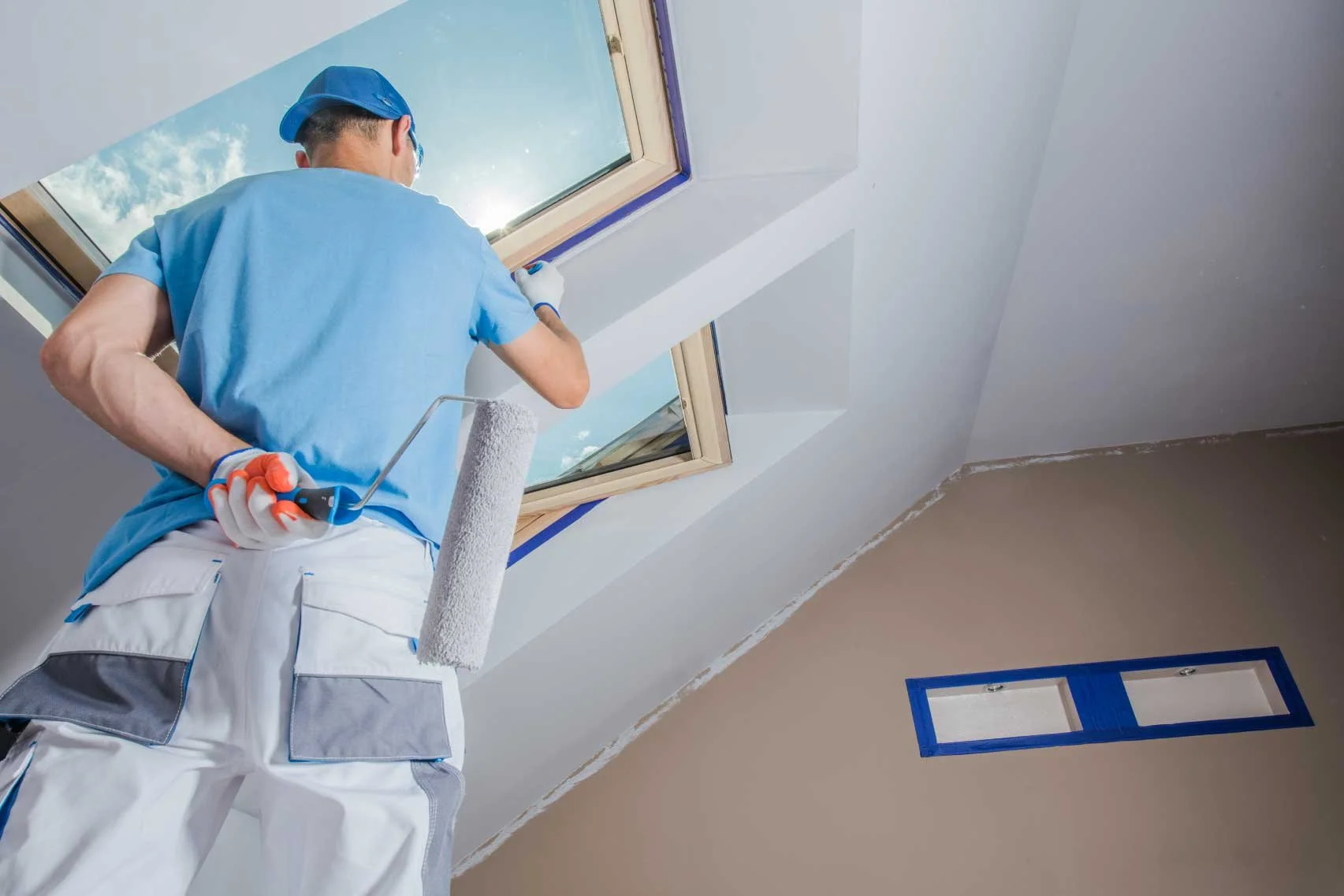 man on ladder painting around skylights in living room