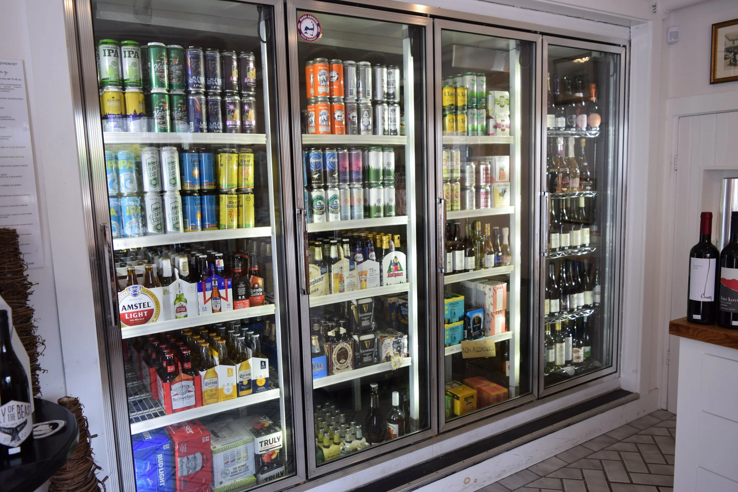 Glass-door refrigerator stocked with various cans and bottles of beer and beverages inside a store.