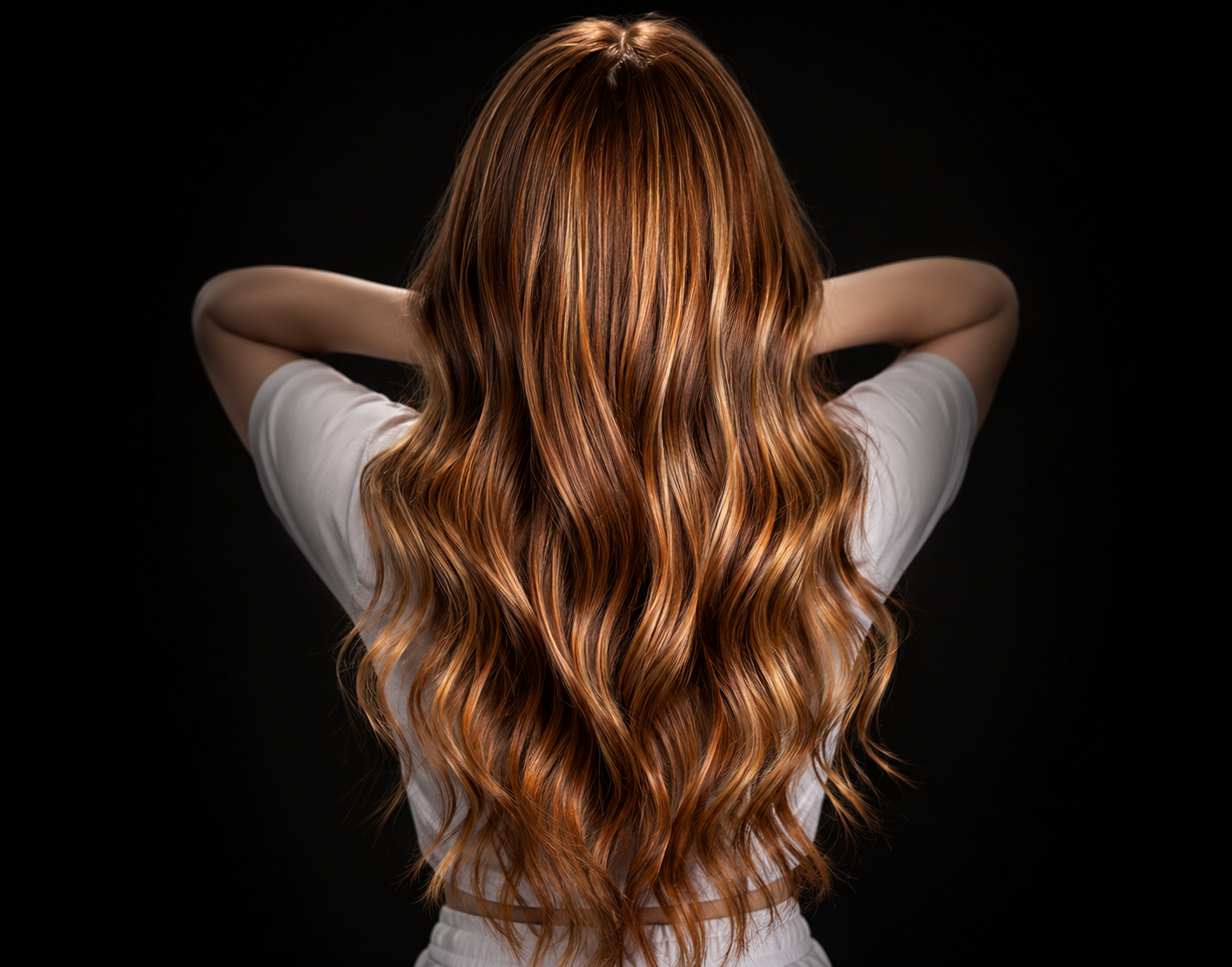 Back view of a woman with long, wavy, reddish-brown hair, wearing a white shirt against a black background.