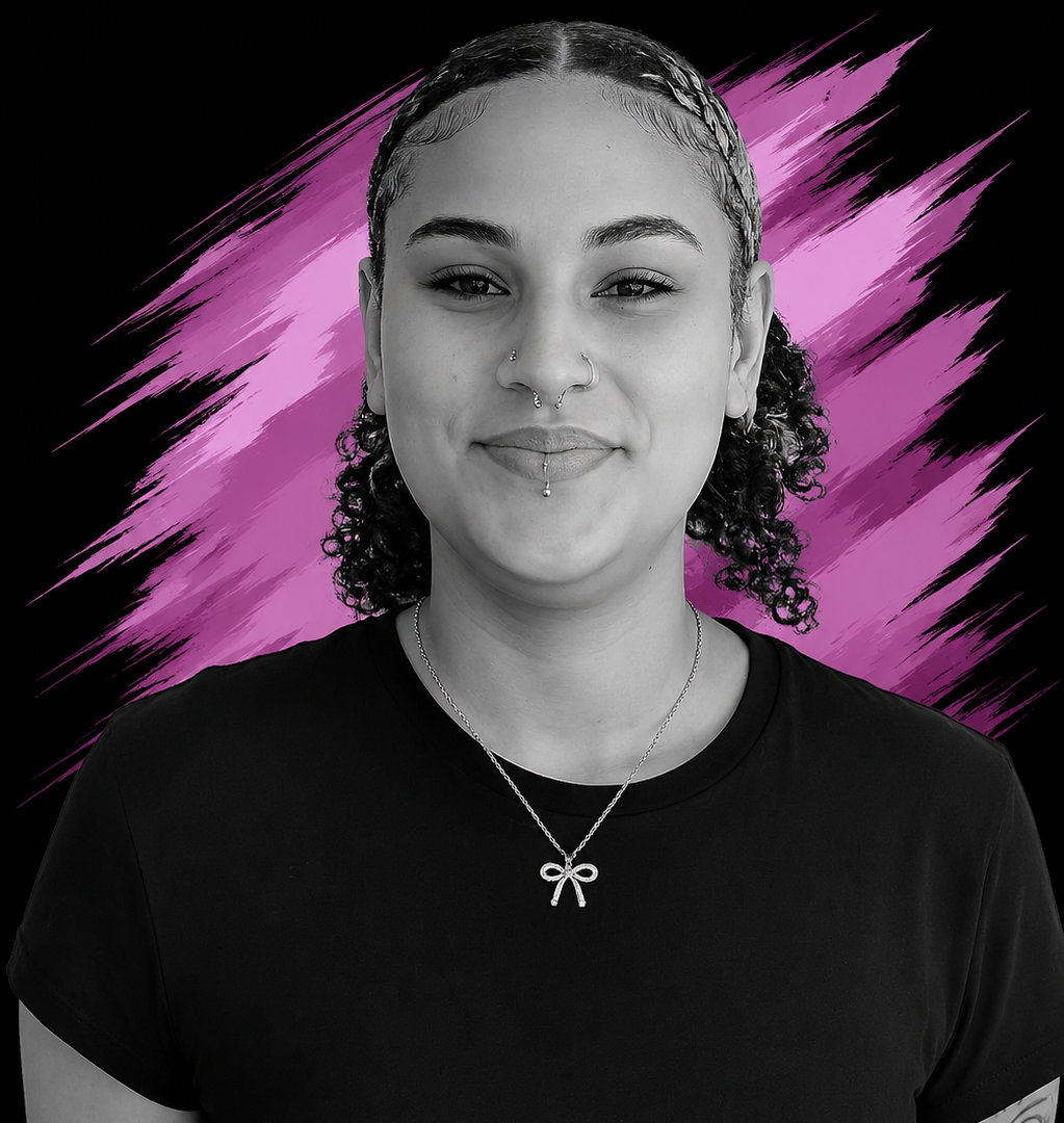 A young woman with curly hair and multiple facial piercings, smiling slightly, wearing a black t-shirt and a necklace with a bow pendant, against a purple and black abstract background.