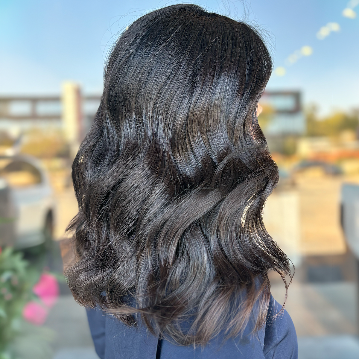Half-length side view of a woman with long, dark, wavy hair outdoors during daytime.