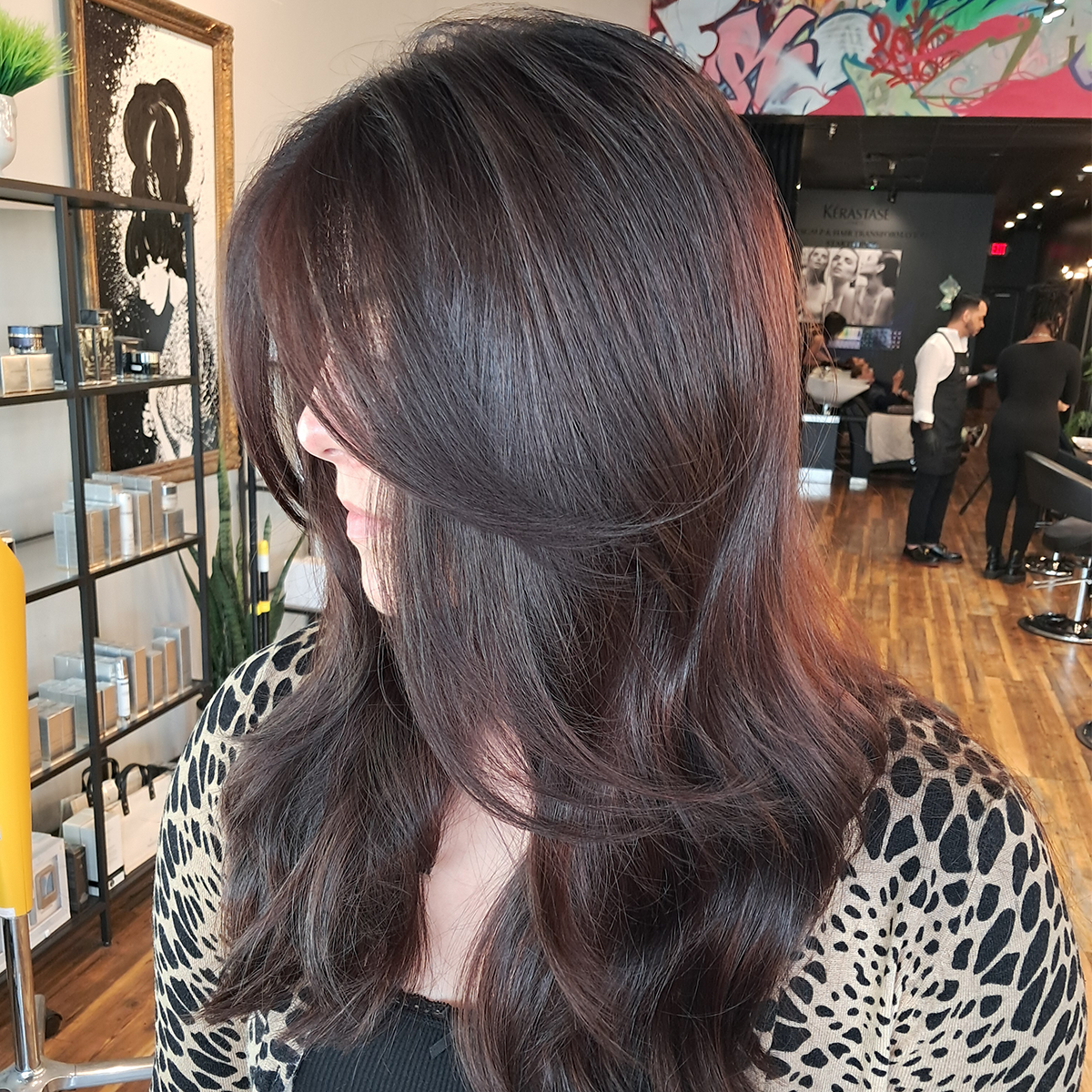 Close-up side view of a woman with long, wavy dark brown hair in a salon.