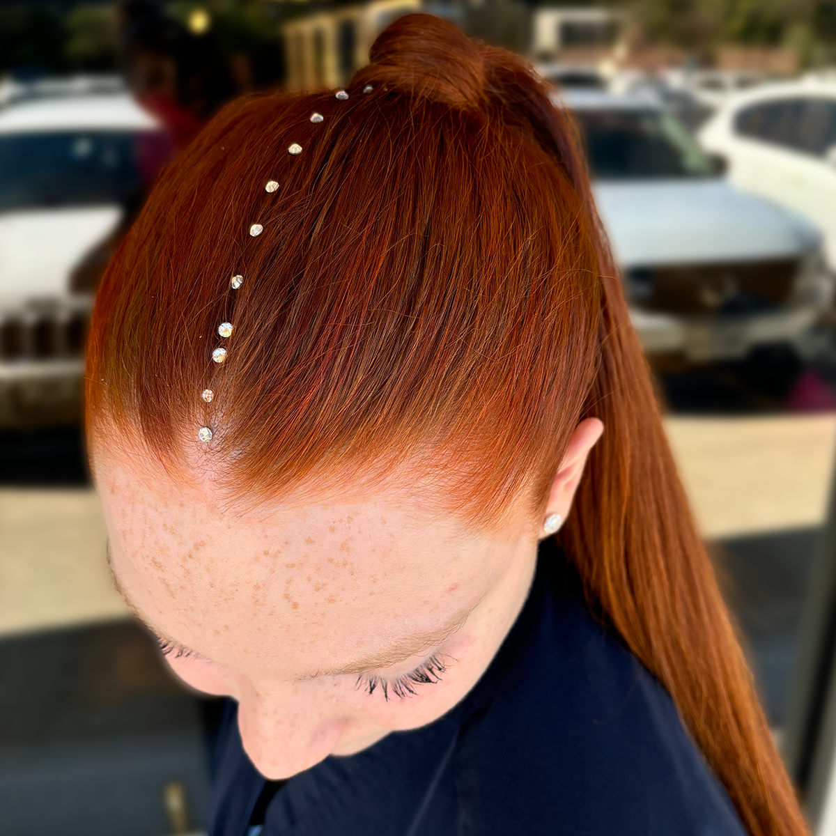 Close-up of a woman with vibrant red hair styled with a rhinestone headband, outdoors in sunlight.