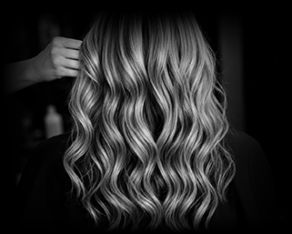 Close-up of a woman with wavy, blonde hair viewed from the back, with hand adjusting her hair.