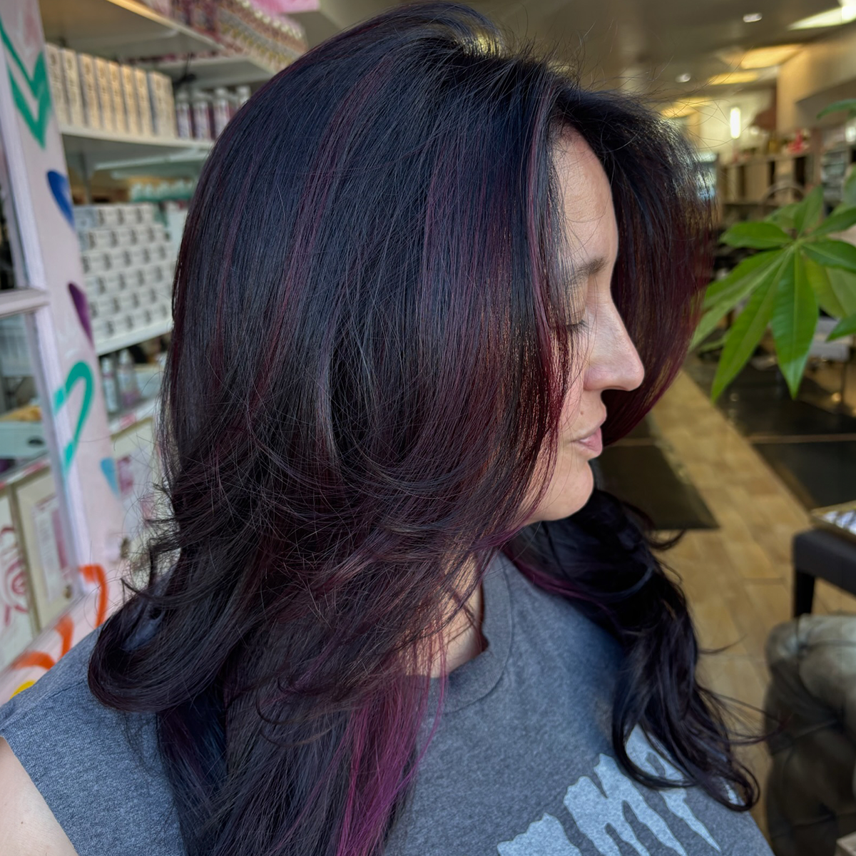 A woman with shoulder-length black hair with purple and pink highlights, viewed in profile inside a store or salon.