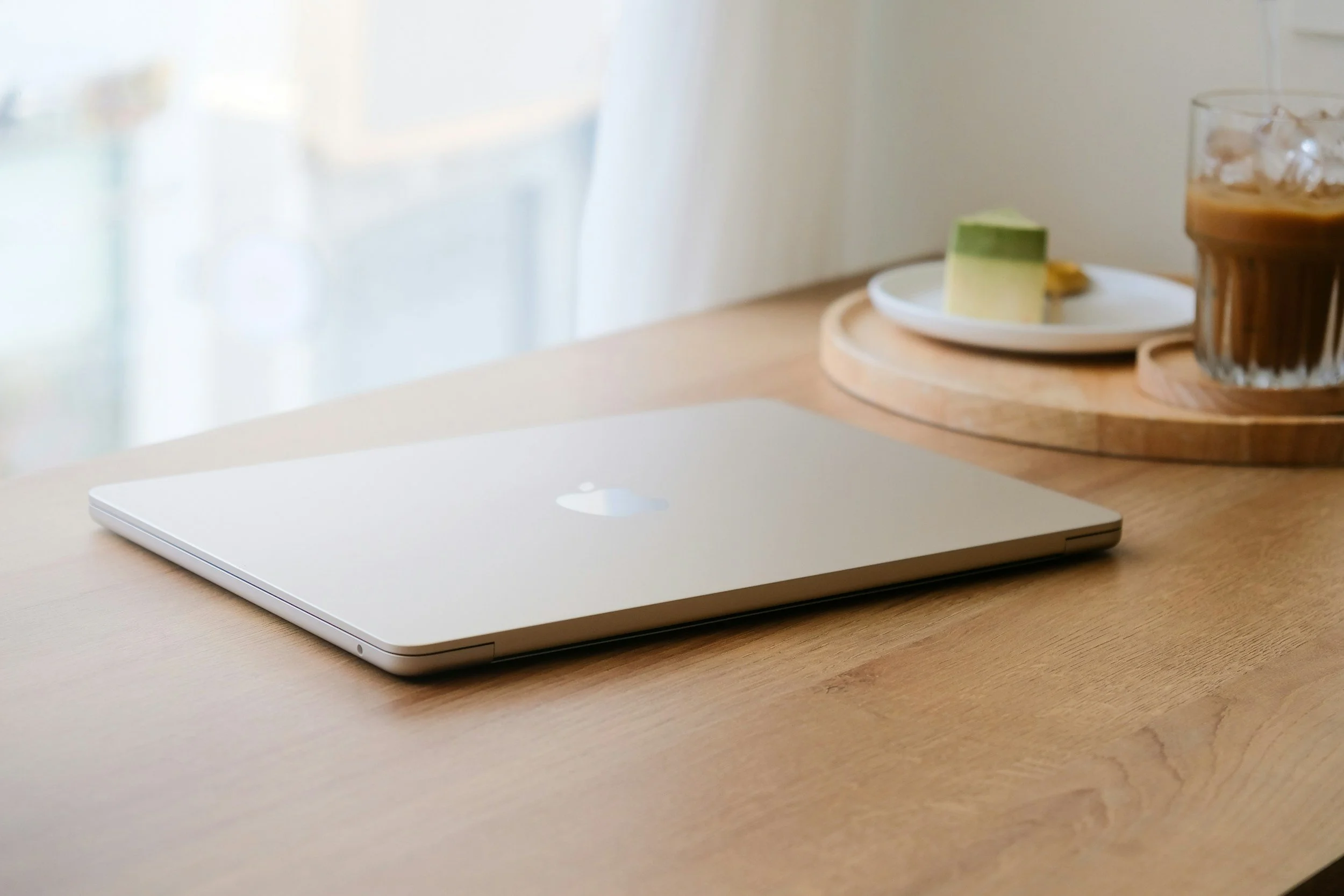 Silver laptop on a wooden desk with a dessert plate and iced coffee