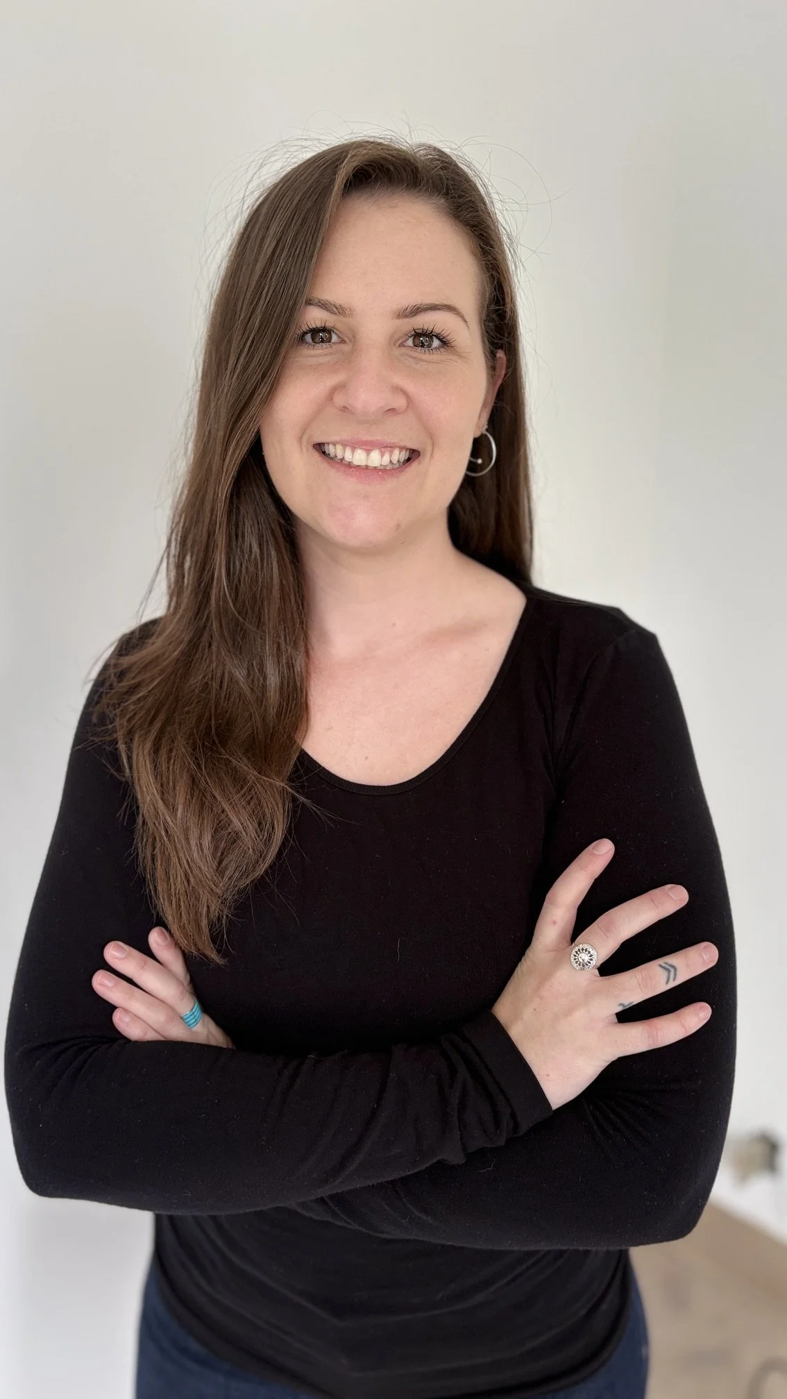 Megan, Marketing and Patient Experience Manager, with long brown hair wearing a black long-sleeve shirt smiling with arms crossed.