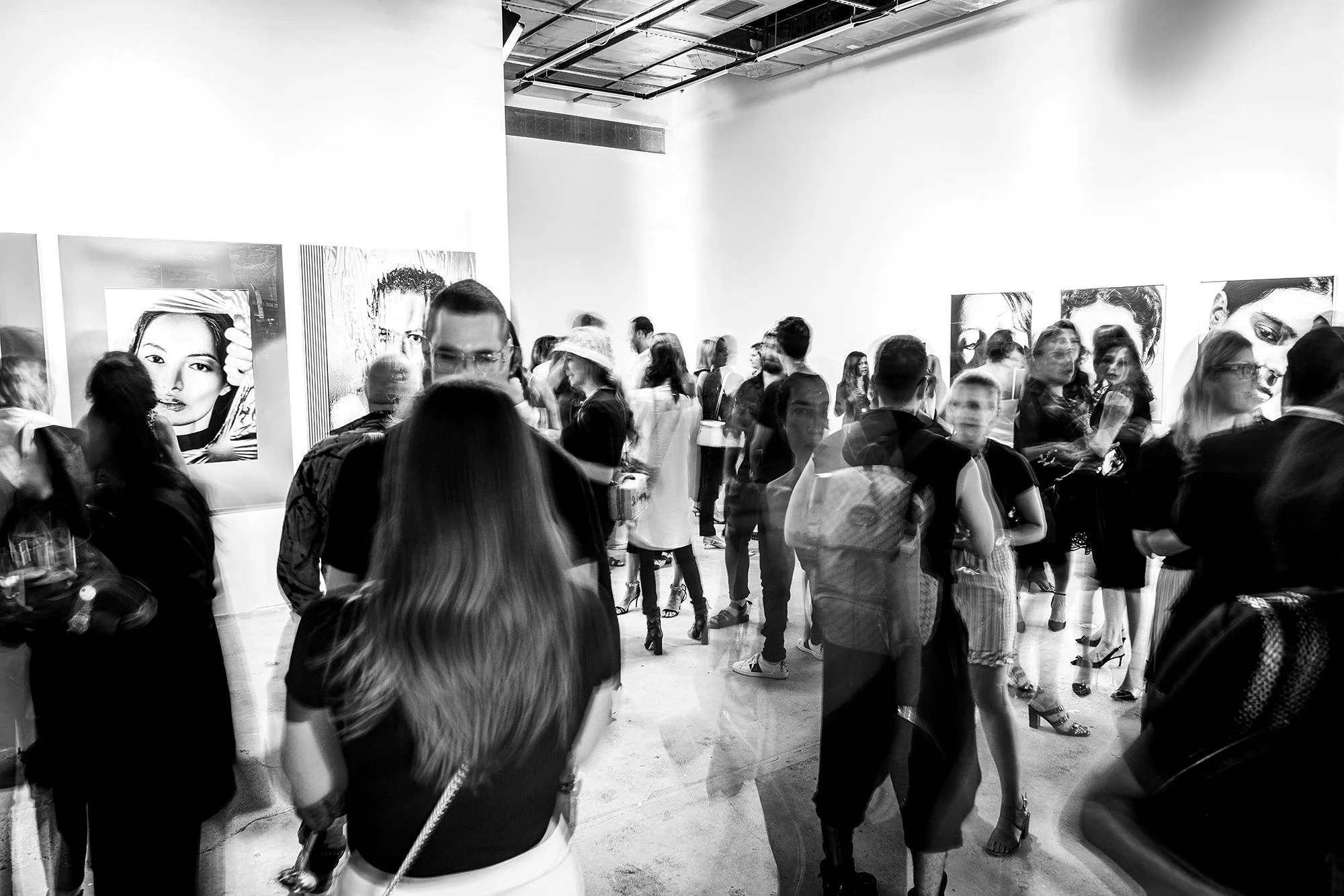 Crowded Los Angeles art gallery opening with guests viewing large portrait paintings