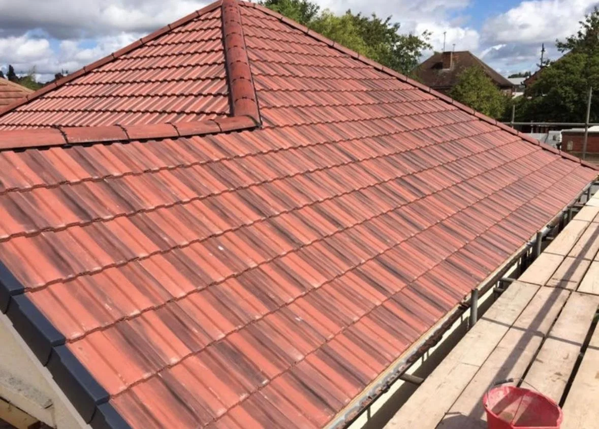 Red tiled roof of a house under construction or repair, with scaffolding and a red bucket nearby.