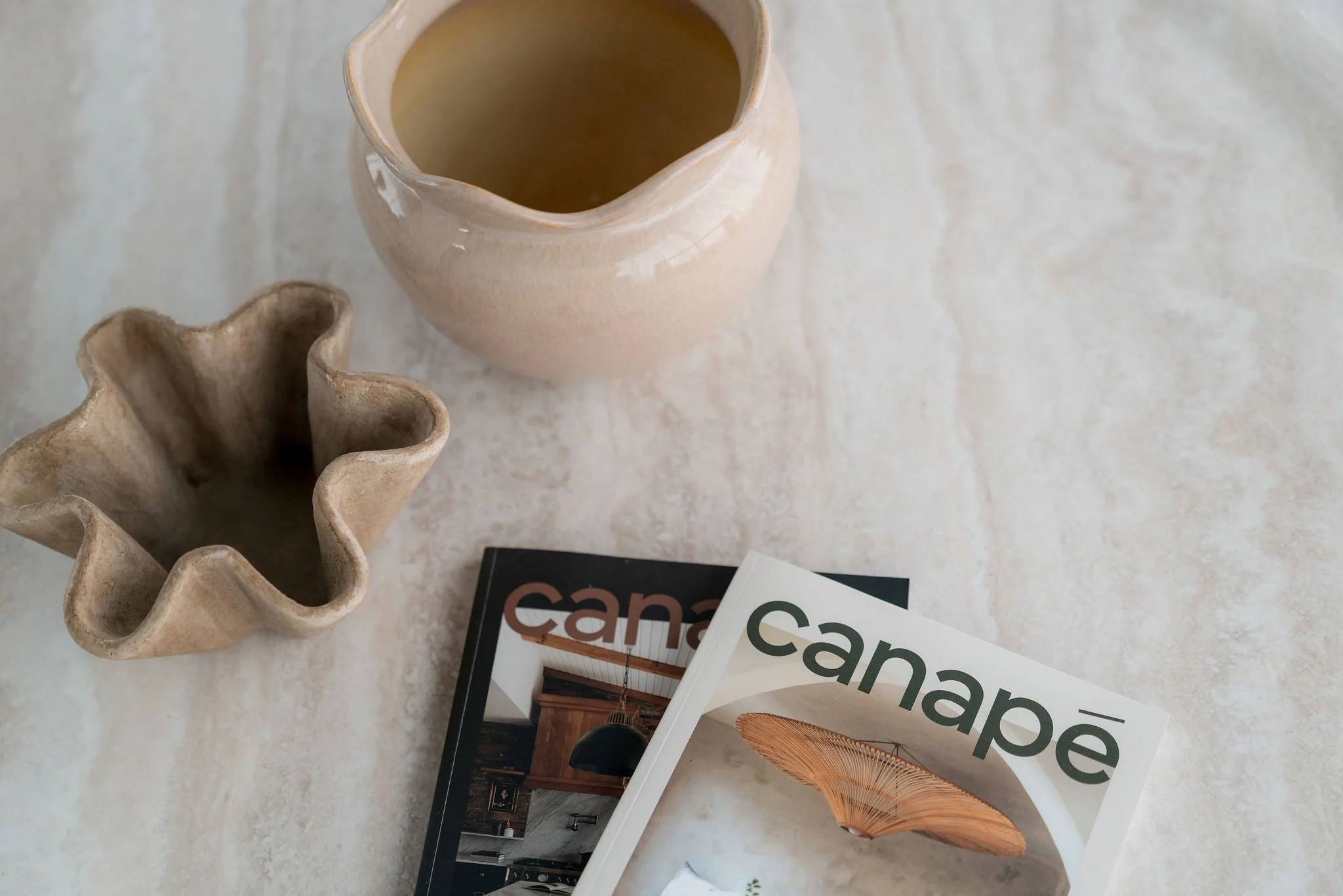 Deux vases en céramique, un beige et l'autre avec une forme ondulée, placés sur une surface claire. Deux livres ouverts portant le mot 'cane' sont également visibles.