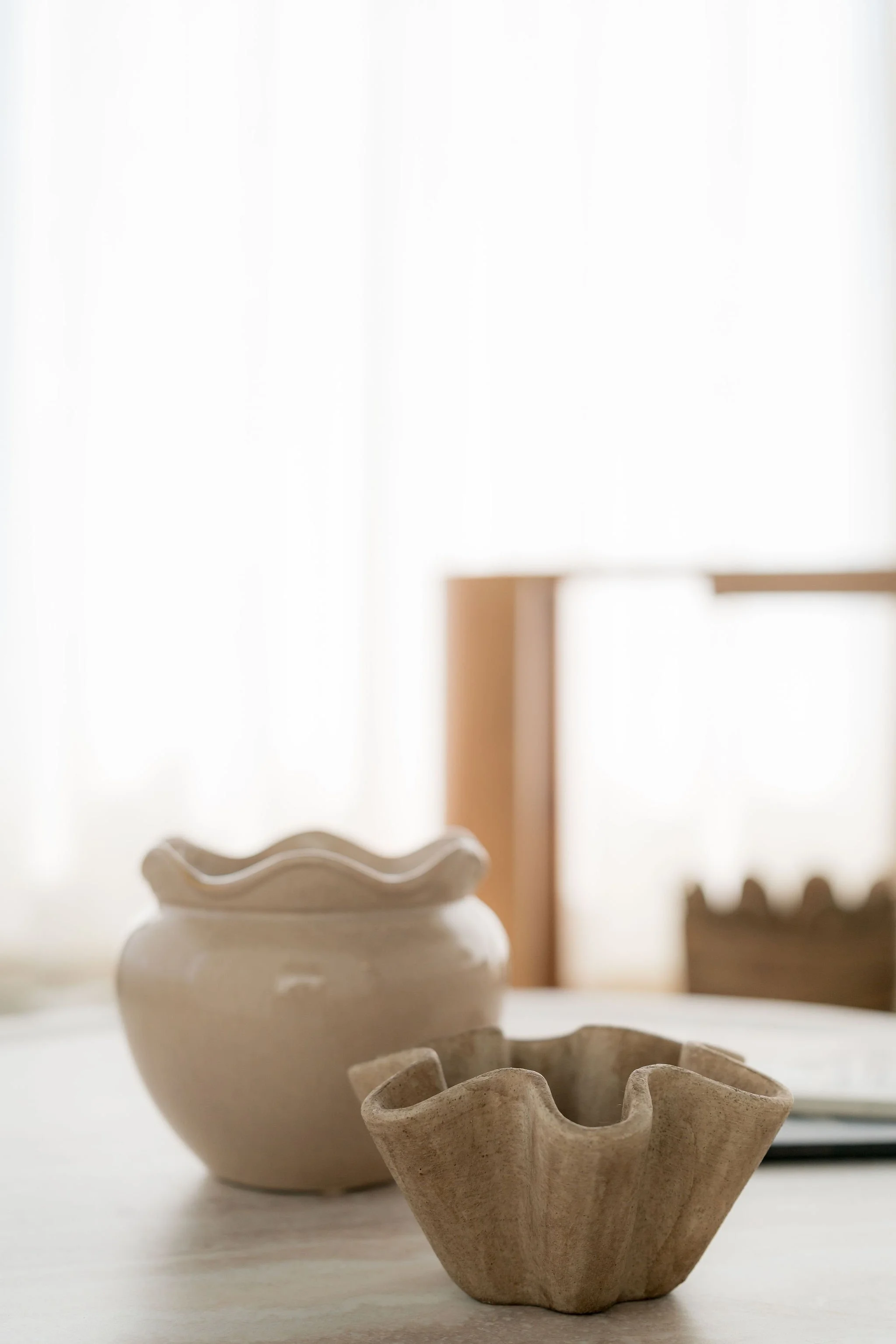 Vases en céramique blanche et beige posés sur une surface en bois, avec une lumière naturelle douce en arrière-plan.