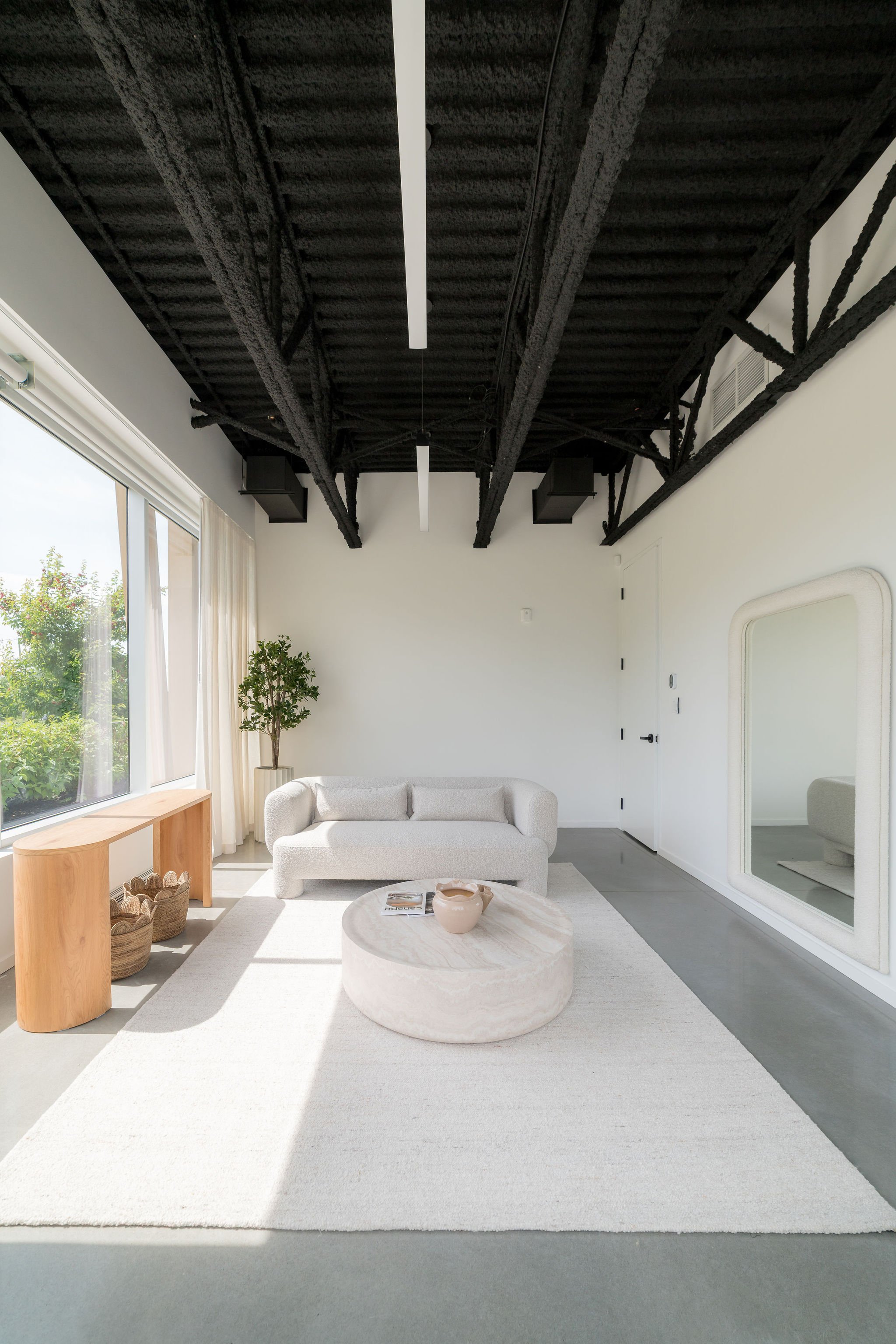 Salon moderne avec plafond noir, canapé blanc, table en marbre, tapis beige, grande fenêtre avec vue sur un jardin, meubles en bois, plantes vertes, miroir mural, décor minimaliste.