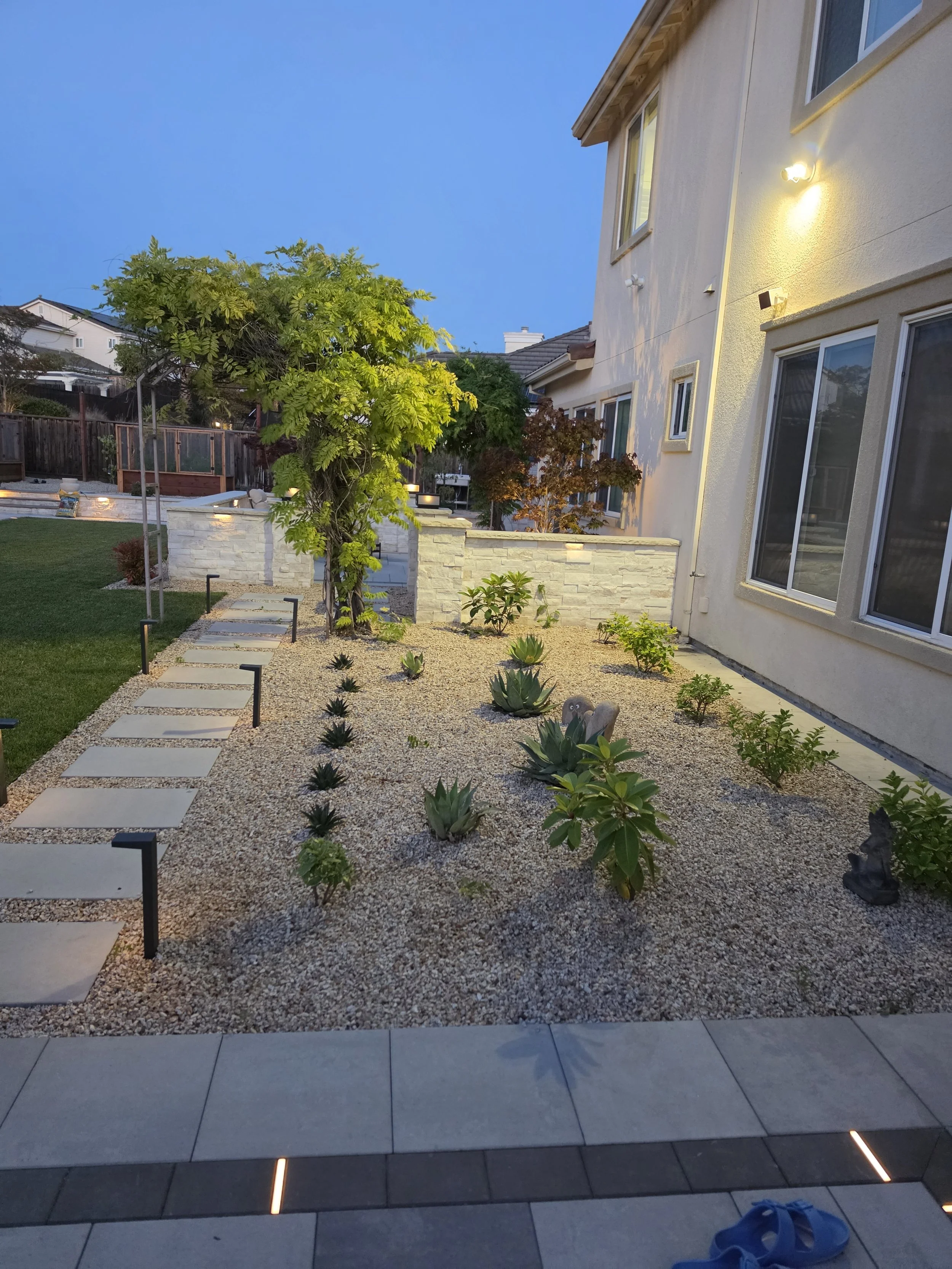 Custom landscape installation featuring a stone pathway, decorative planting, landscape lighting, and modern hardscape elements designed to enhance curb appeal and outdoor functionality.