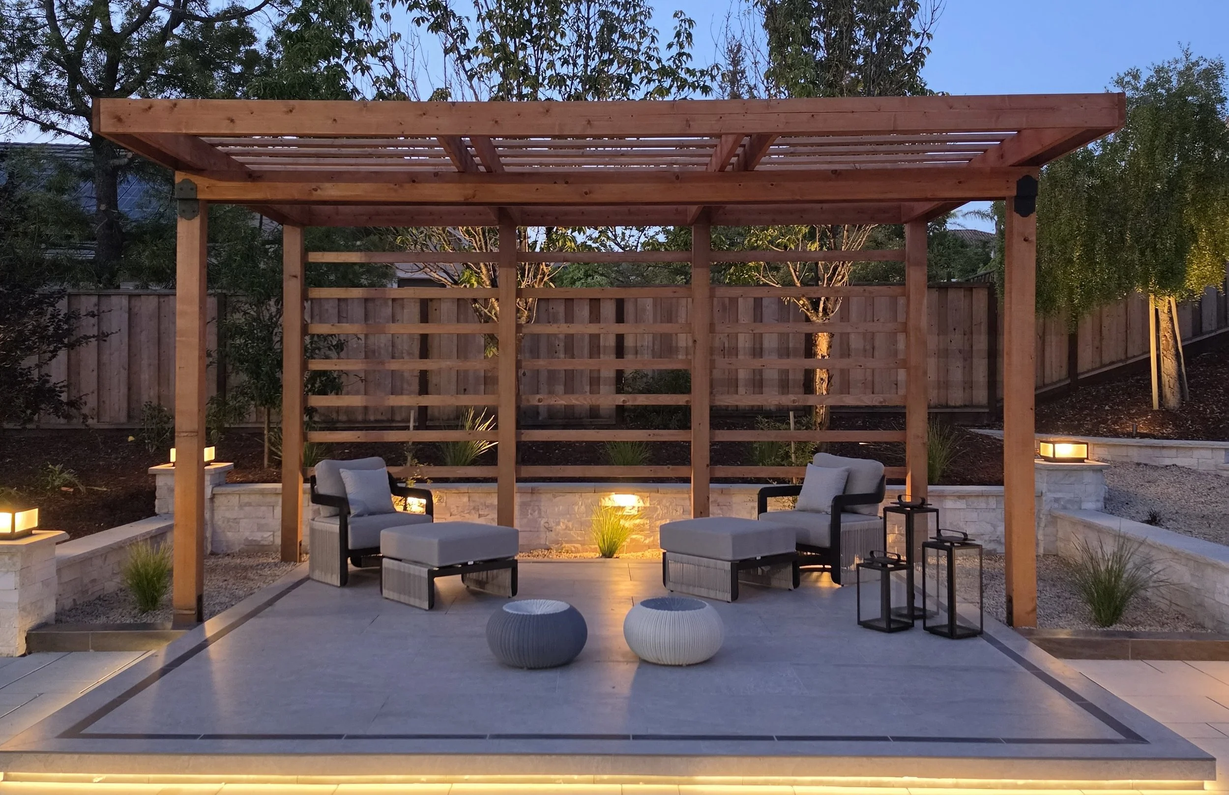 Custom wood pergola with outdoor seating area, hardscape patio, landscape lighting, and surrounding landscaping designed for outdoor living and entertainment.