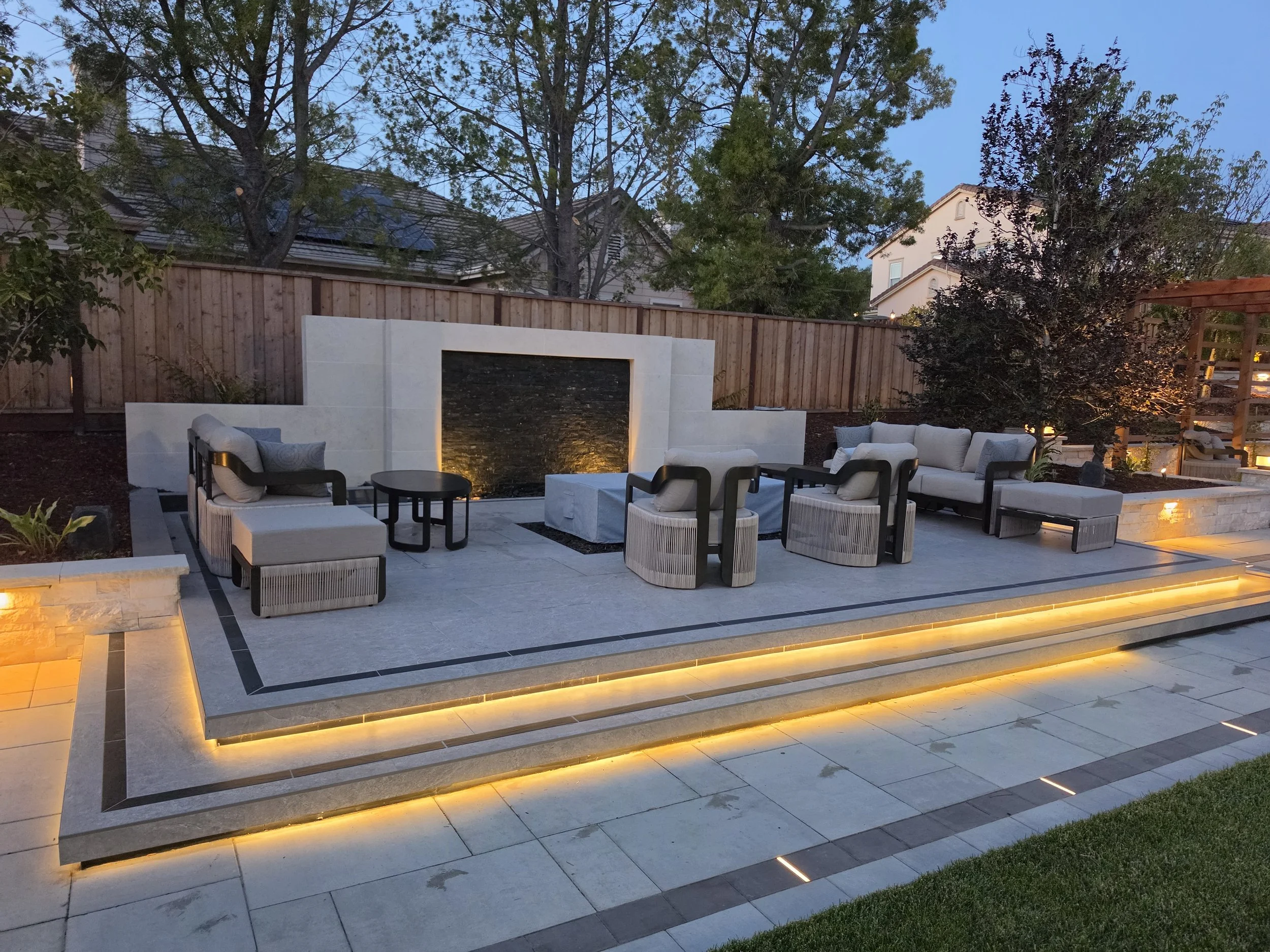 Custom hardscape patio with built-in fireplace, retaining walls, landscape lighting, and outdoor living space designed for year-round entertaining.