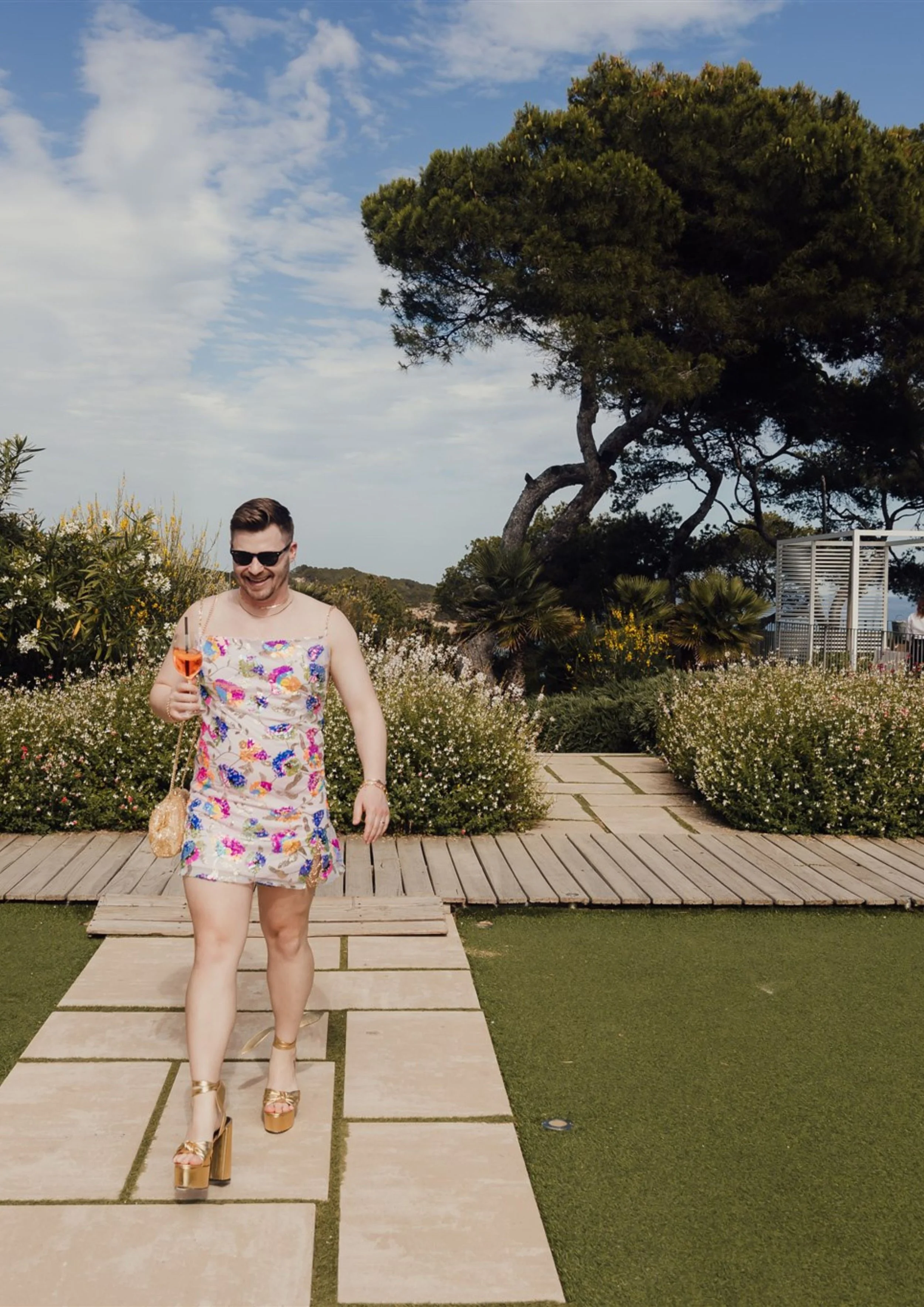 portrait of a man in a dress with gold platforms walking with a cocktail at a destination wedding by Jo Kemp Photography