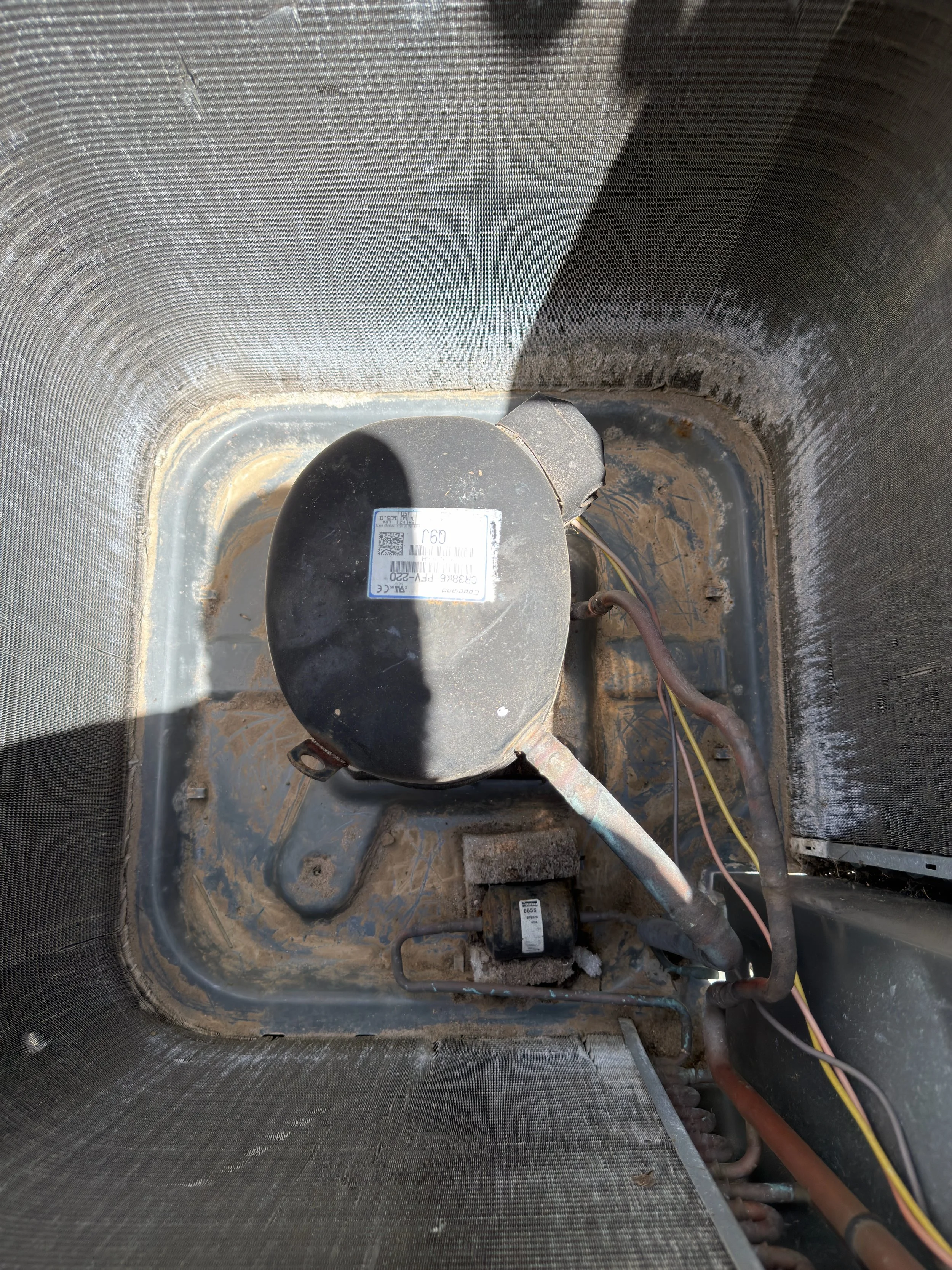 Inside of an air conditioning unit with visible wiring, compressor, and tubing.