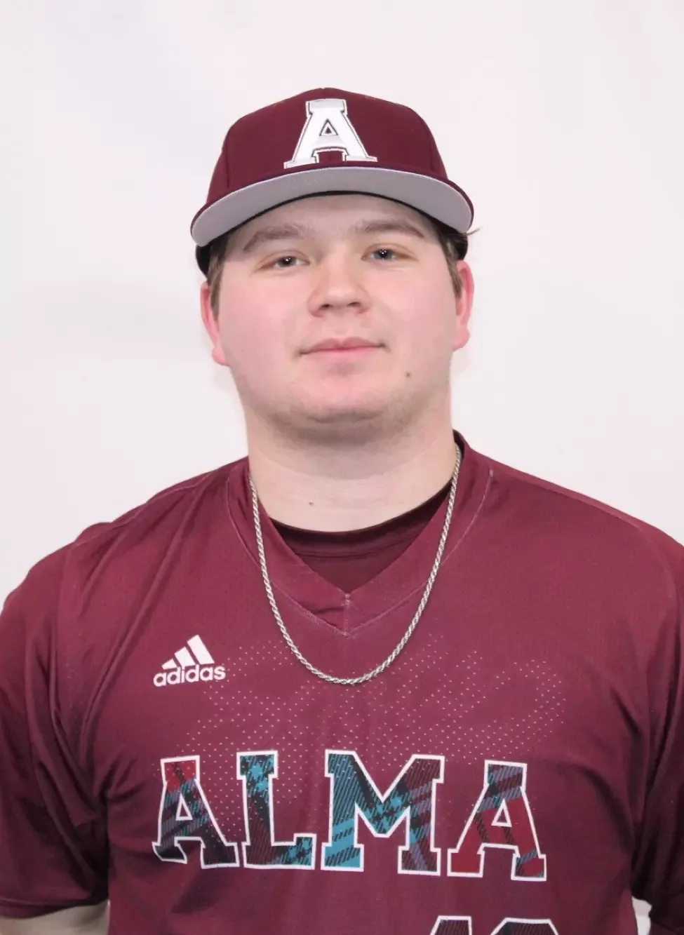 Colin Danek college pitcher wearing a maroon Alma baseball jersey, a matching maroon and gray cap, a silver chain, posing against a plain white background.