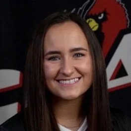 Young woman with long brown hair smiling, in front of an Arizona Cardinals logo background.