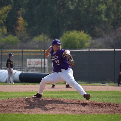 Colin Danek, a college baseball pitcher in a purple uniform, is throwing a pitch on a baseball field.