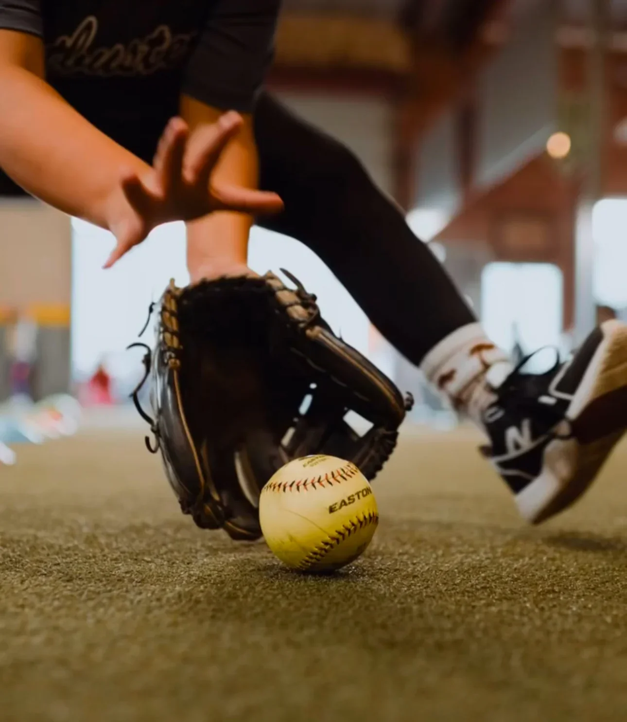 Close-up of a person in a black glove catching a baseball with a baseball glove on a field, with the ball near the ground.
