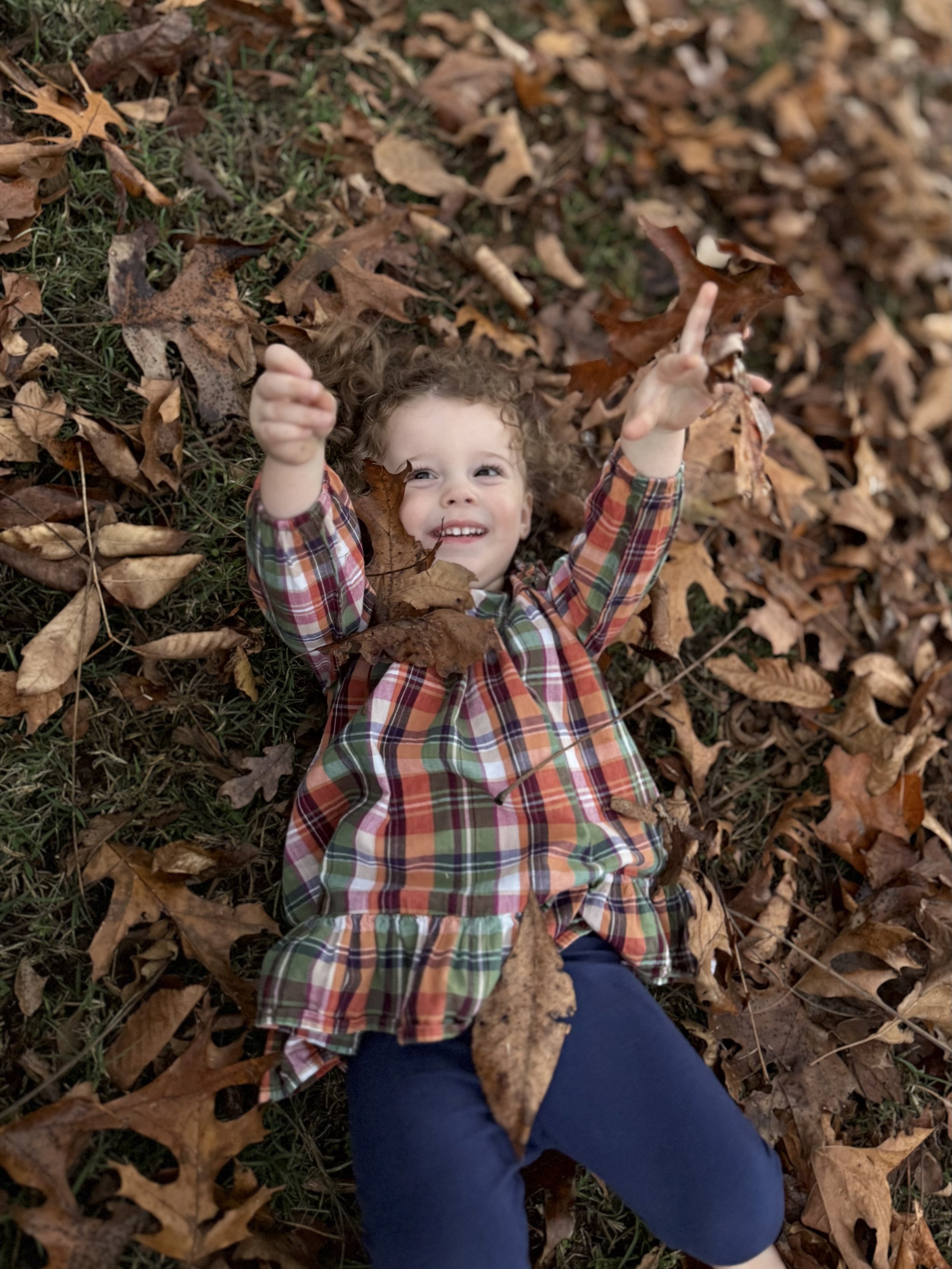 A child playing in fallen leaves during a sensory-based outdoor activity with Rooted Kids Therapy.