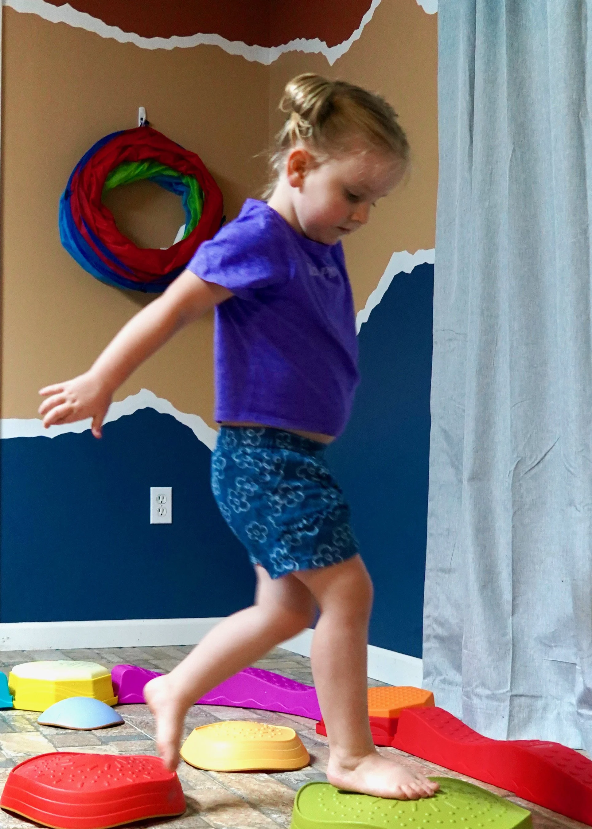 Young girl building balance and gross motor skills on stepping stones during an in-home pediatric OT session in Mountain Home, AR.