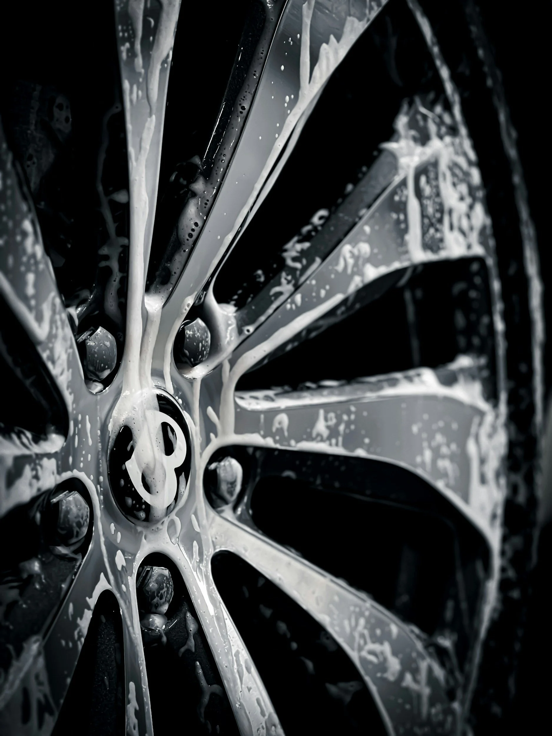 Close-up of a black car wheel being washed with soap and water, showing shiny rim and soap suds.