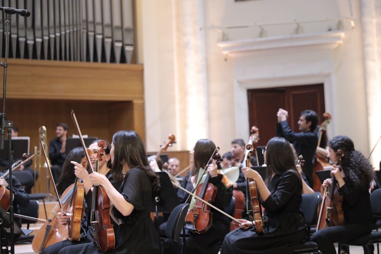 Orchestra of musicians playing string instruments in a concert hall.