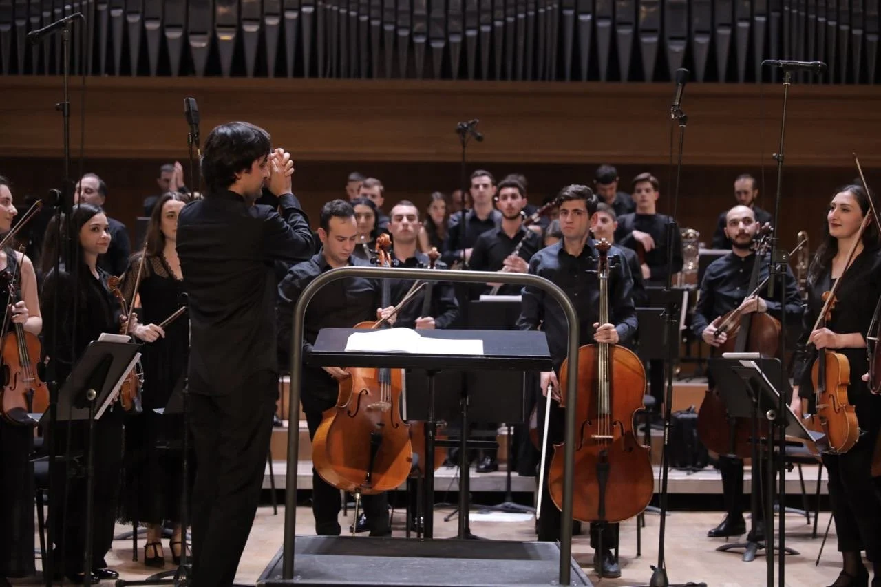 Orchestra conductor and musicians on stage, holding string instruments in a concert hall.