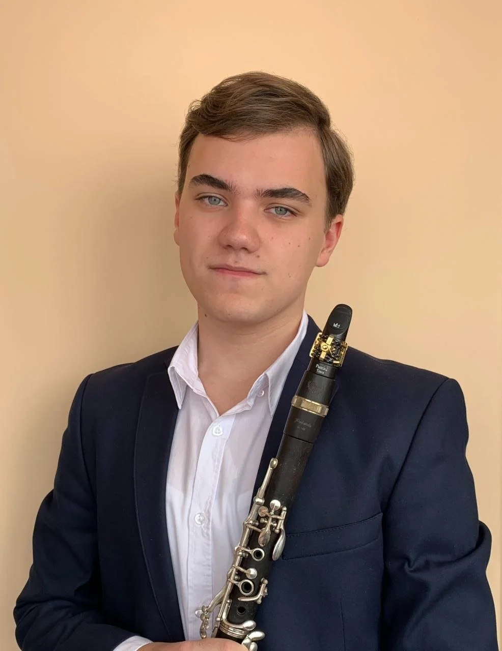 Young man in a dark suit holding a clarinet.