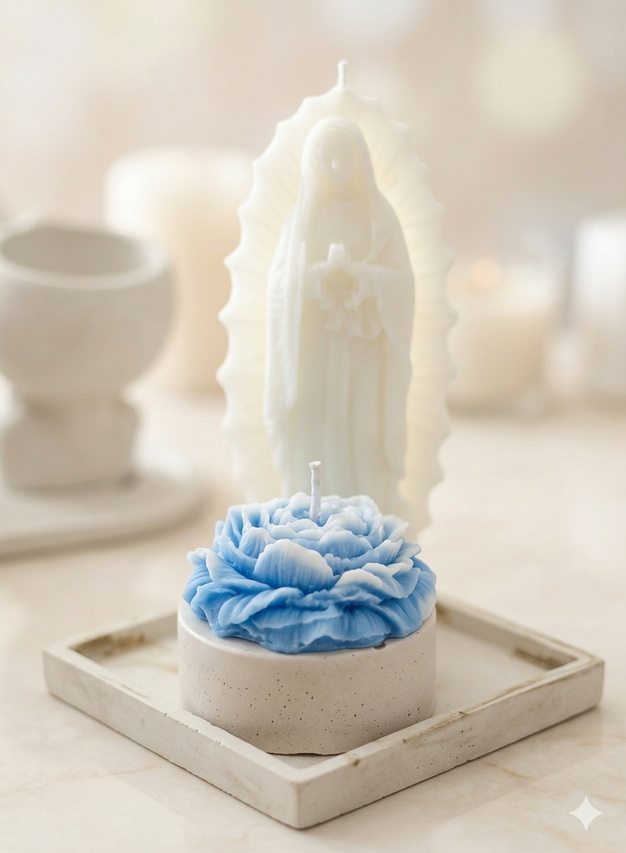 Velas decorativas blancas y una vela en forma de flor azul en un recipiente de cemento, con una figura de la Virgen María de tamaño pequeño en fondo borroso.