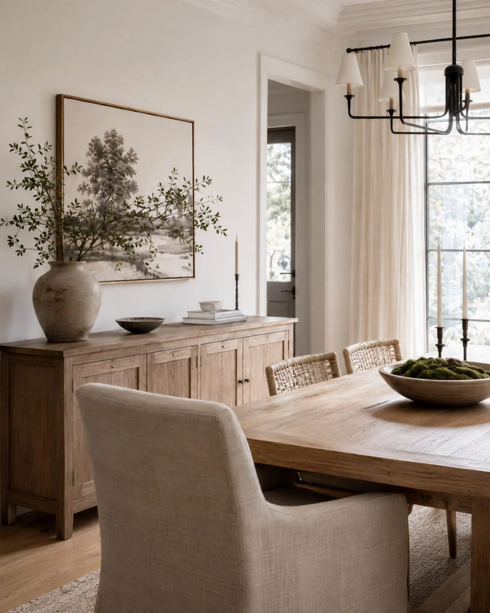 A dining room with light wood furniture, a large wooden sideboard, decorative vases, a framed botanical print on the wall, a chandelier with covered bulbs, and large windows with cream pinch pleat TwoPages curtains on sale with discount code GLOW.