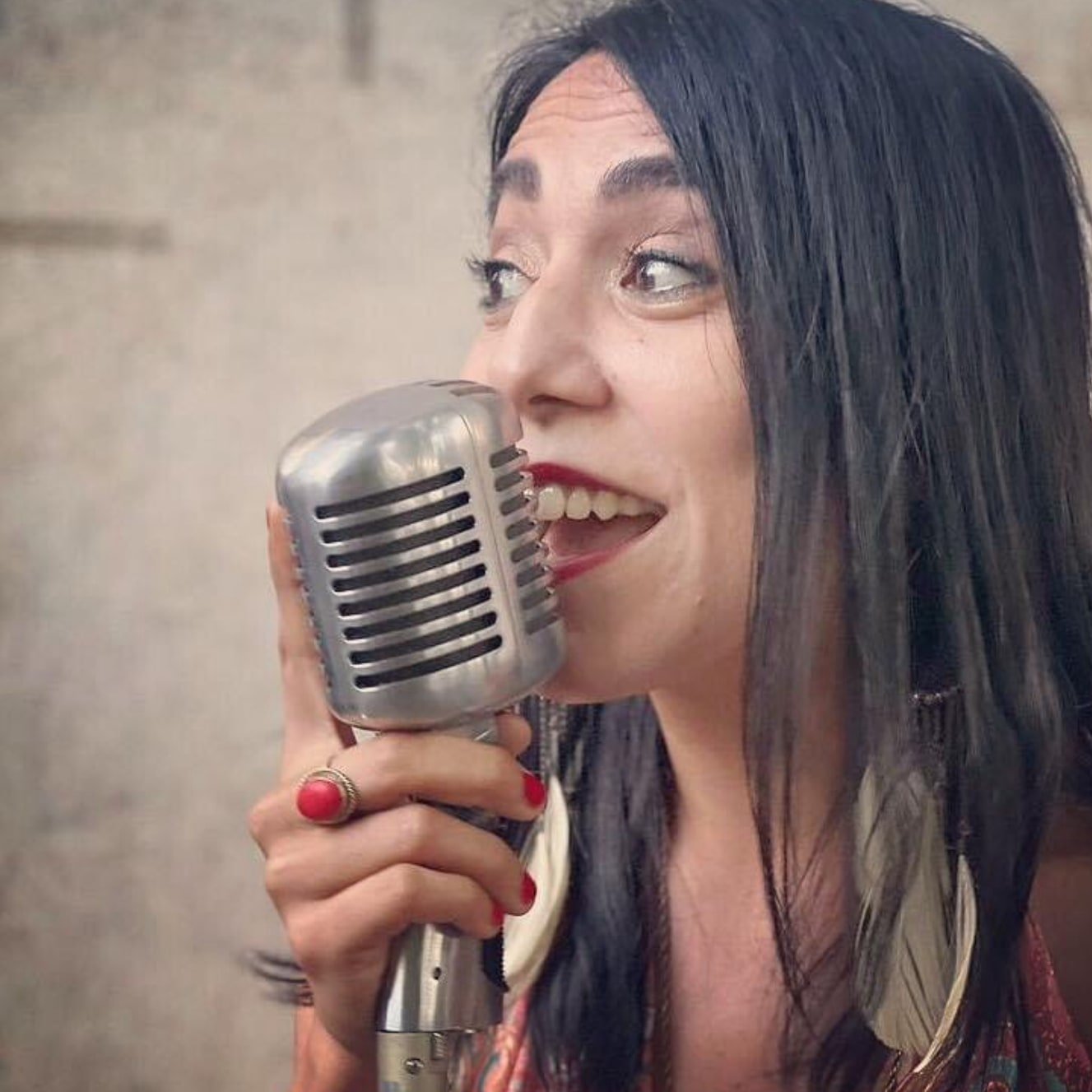 A woman with long black hair singing into a vintage silver microphone.