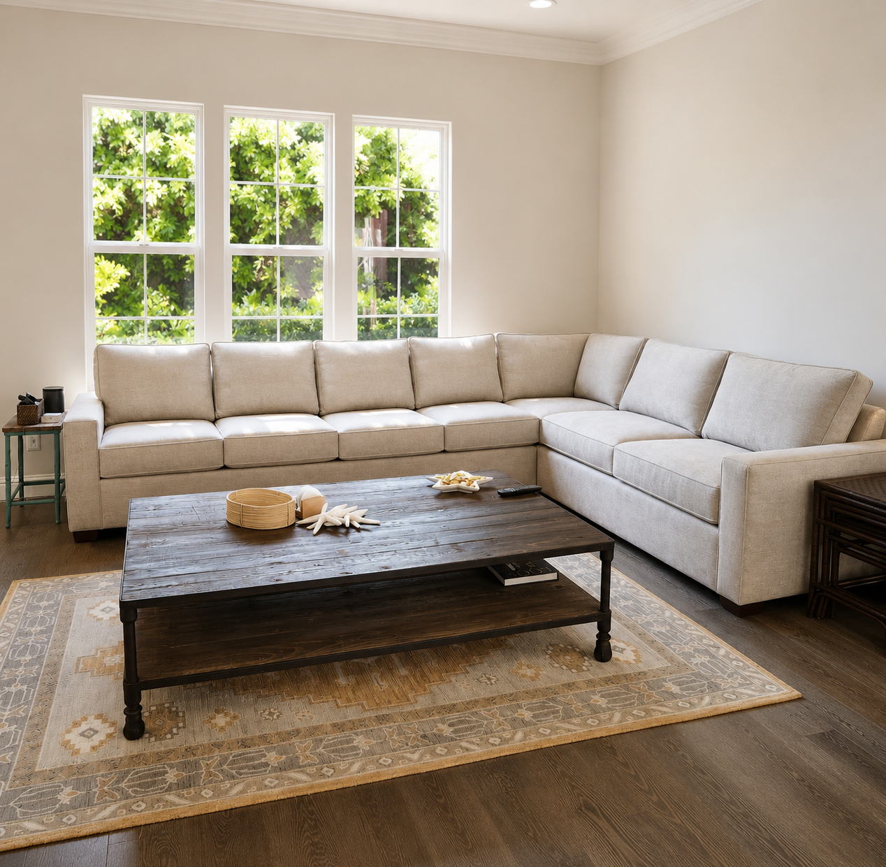 Living room with beige sectional sofa, wooden coffee table, window with greenery outside, and decorative rug.