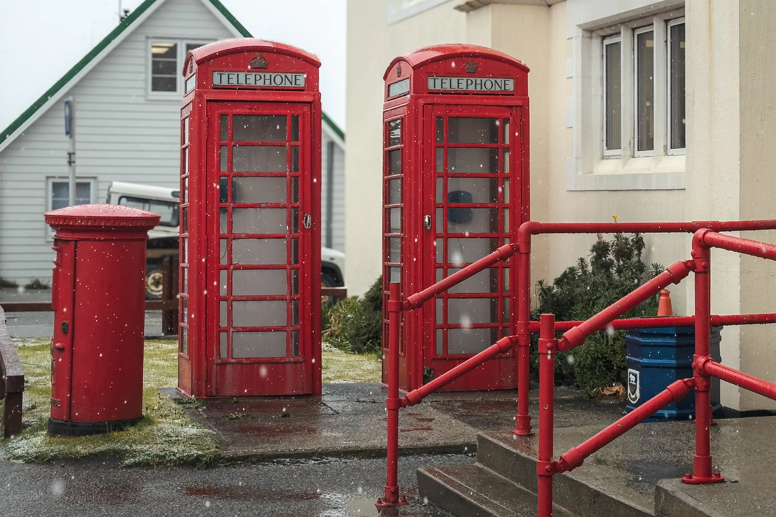 Two classic red British telephone booths next to each other outside a building on a rainy day.