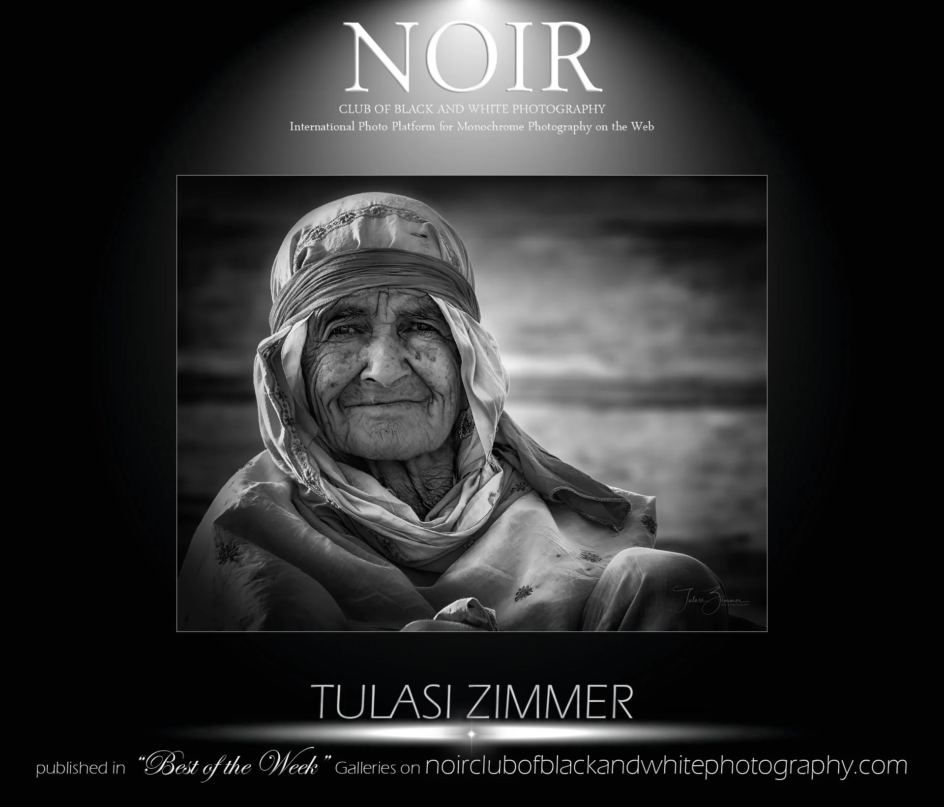 Black and white portrait of an elderly woman with a headscarf, smiling with visible wrinkles, against a cloudy sky background.