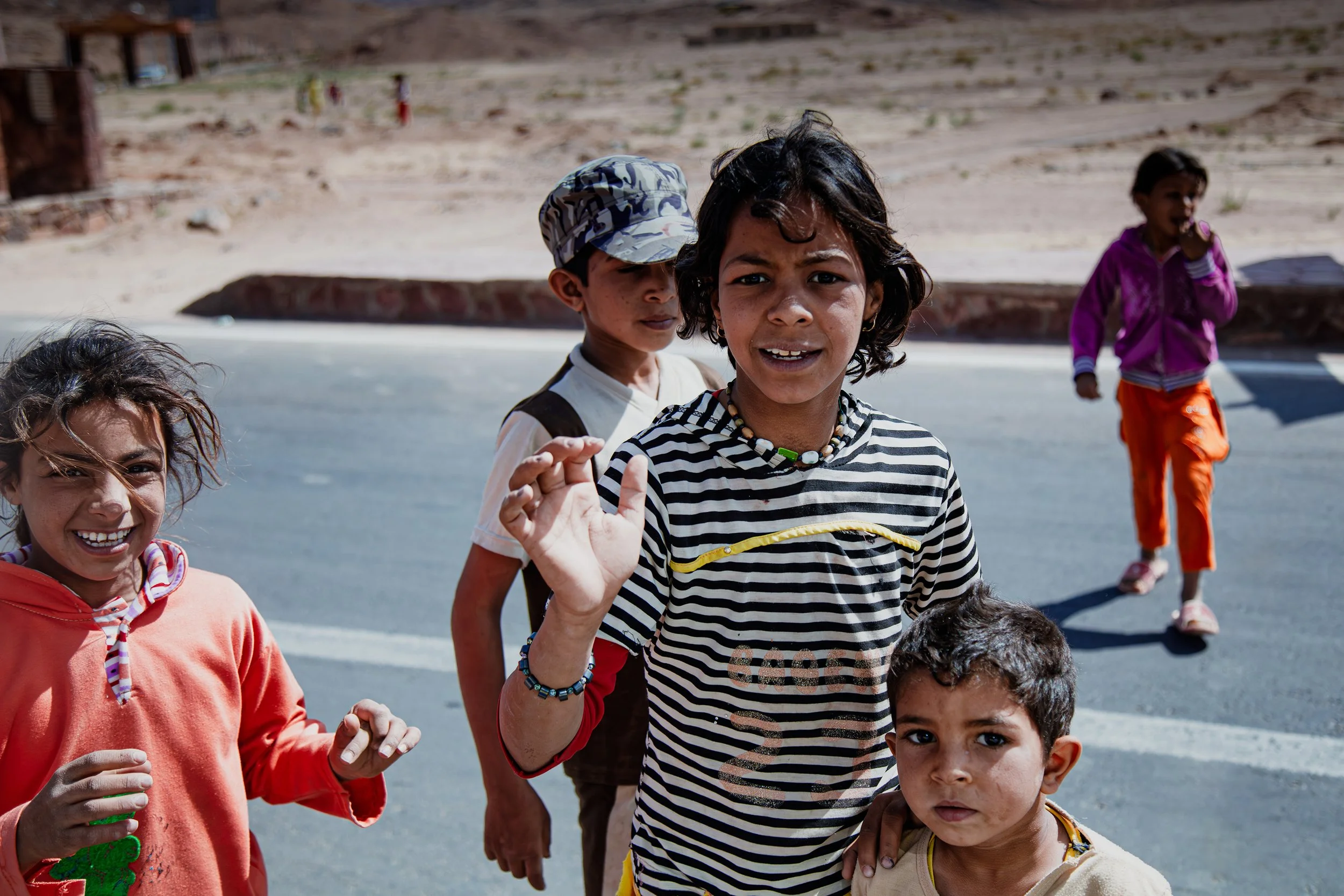 Group of Egyptian children smiling and posing for the camera outdoors. The background shows a desert landscape with hills and sparse vegetation.