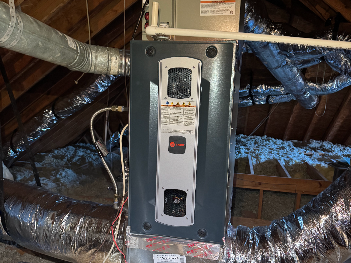 HVAC furnace unit installed in an attic with insulation and ductwork.