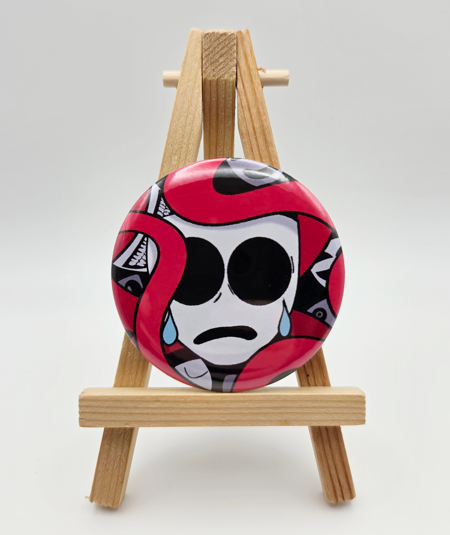 A button featuring GANGLE from THE AMAZING DIGITAL CIRCUS resting on a small easel.